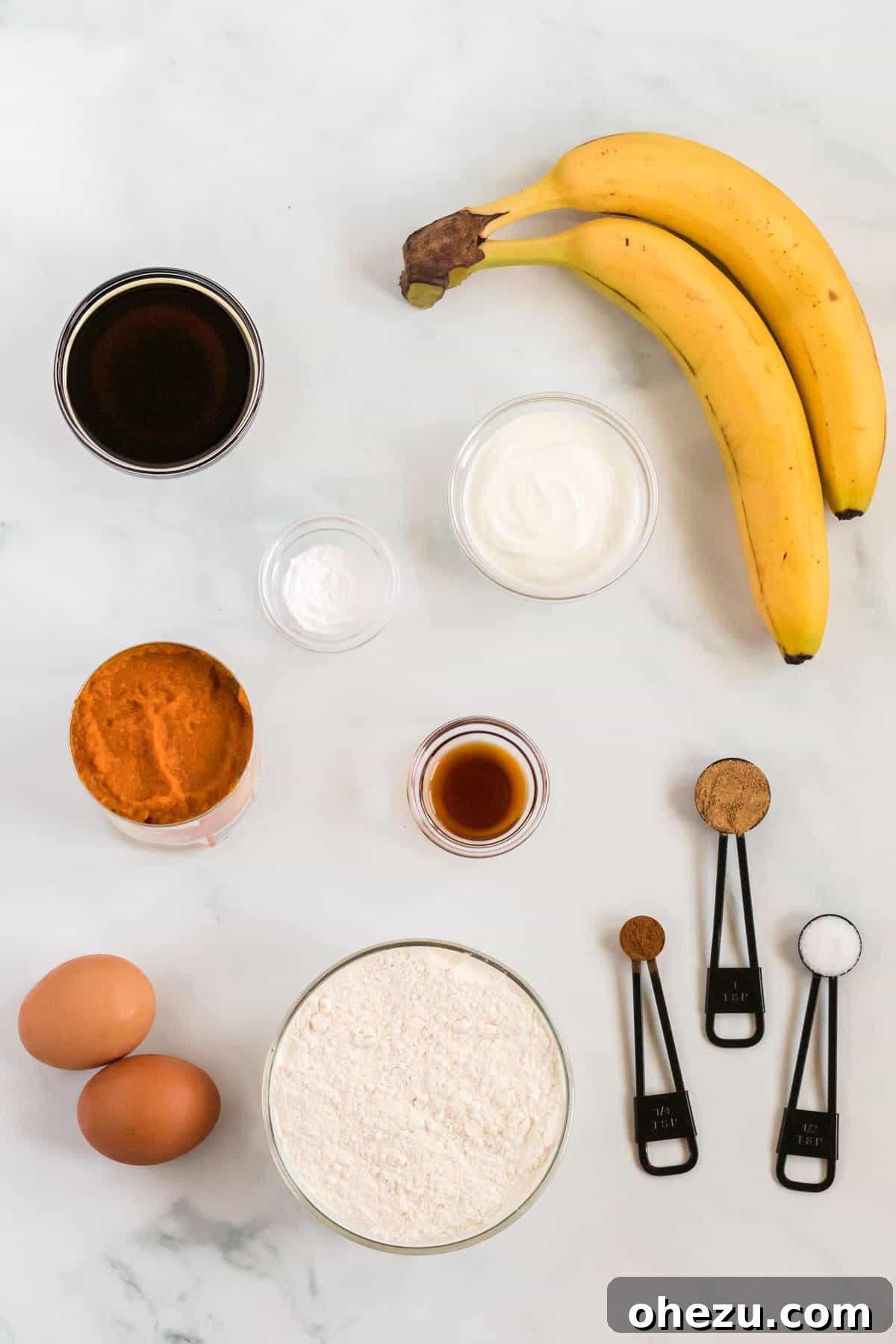 A collection of fresh ingredients laid out on a table, including bananas, a can of pumpkin, and a bowl of Greek yogurt, ready to be transformed into healthy pumpkin banana bread.