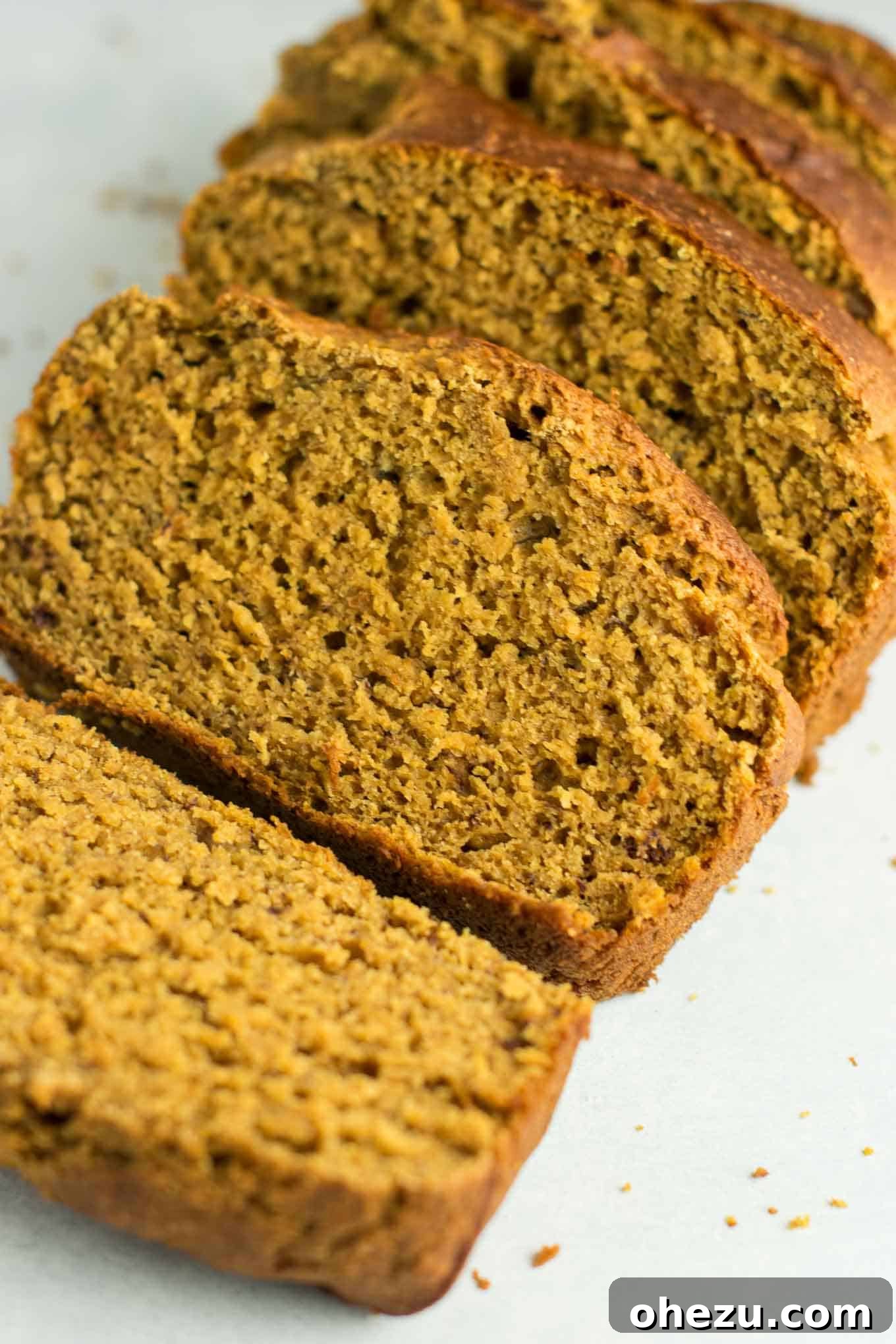 Close-up of three delicious slices of healthy pumpkin banana bread stacked on a rustic cutting board, highlighting the soft texture and speckles of spice.