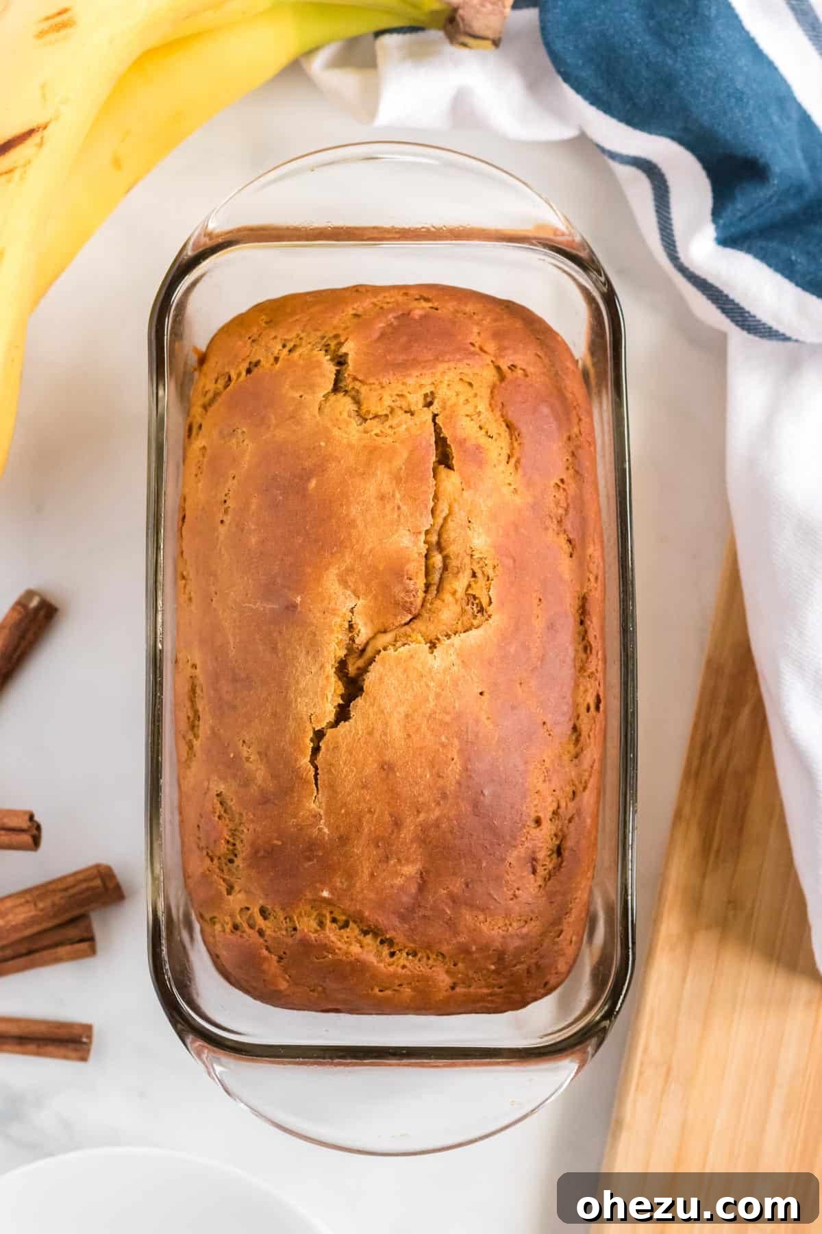 A golden-brown loaf of healthy pumpkin banana bread, fresh out of the oven, cooling in its loaf pan.