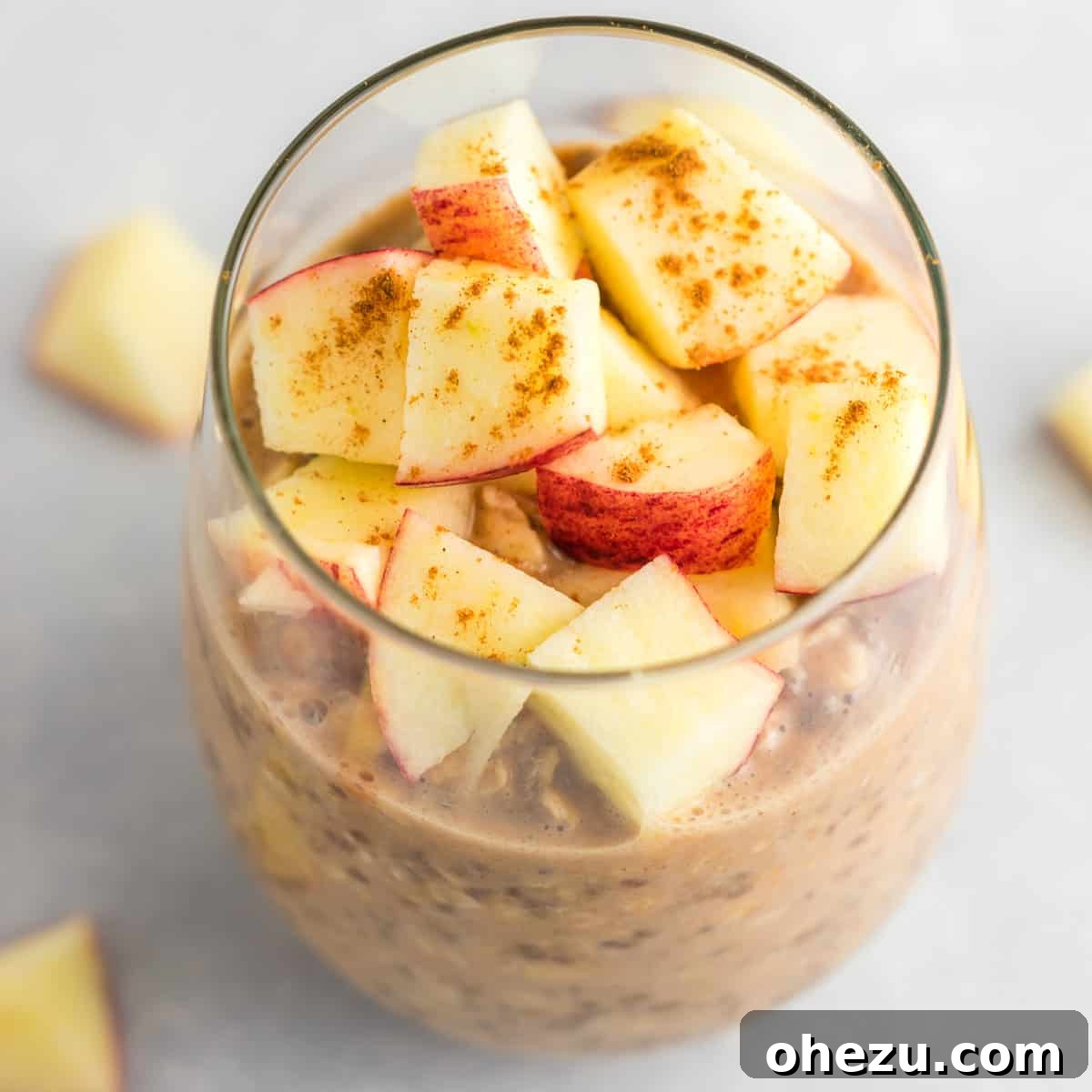 A glass jar filled with creamy apple cinnamon overnight oats, topped with fresh diced apples and a sprinkle of ground cinnamon, ready to eat.
