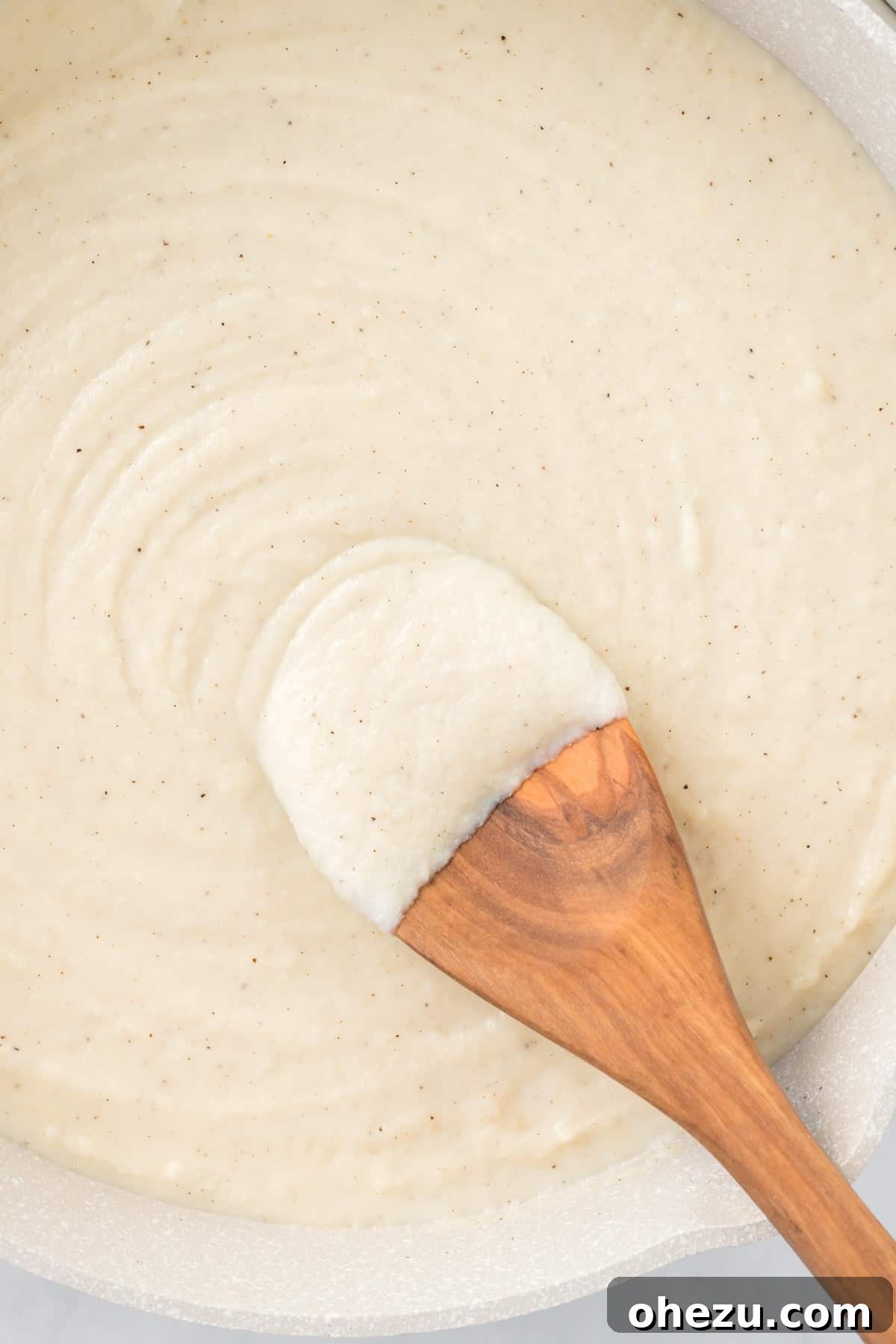 wooden spoon dipped in cauliflower alfredo sauce