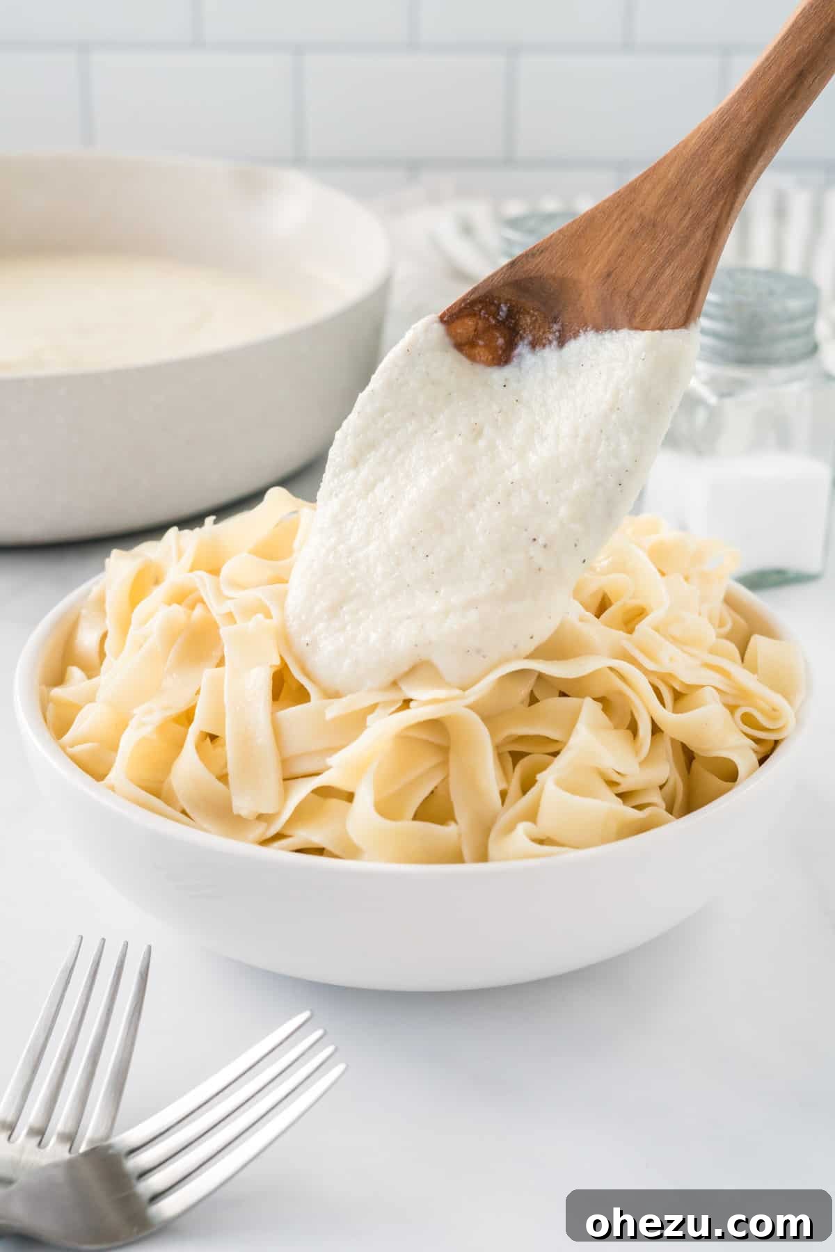 pouring cauliflower Alfredo sauce over a bowl of fettuccini noodles