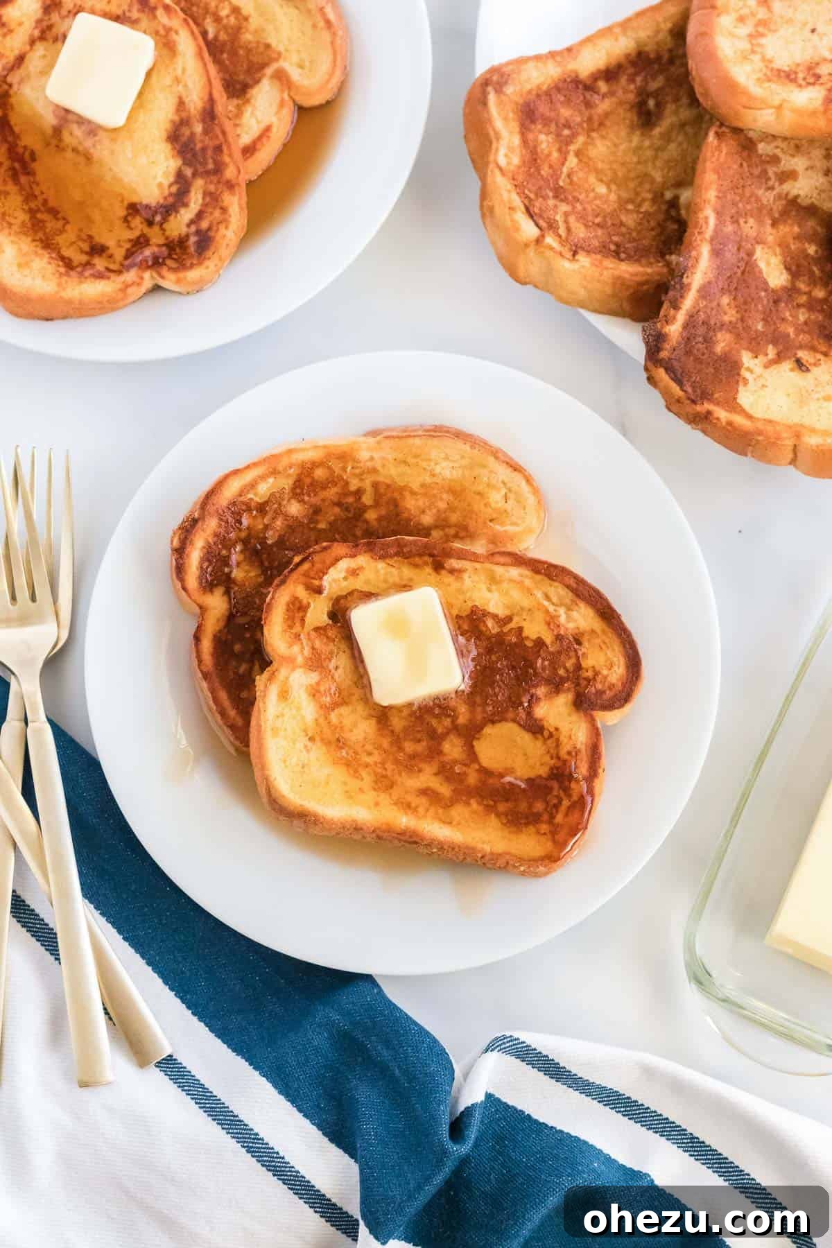 Festive Eggnog French Toast 2 Delicious eggnog French toast on a plate topped with melted butter, a generous pour of maple syrup, and a light dusting of powdered sugar, garnished with a sprig of rosemary.