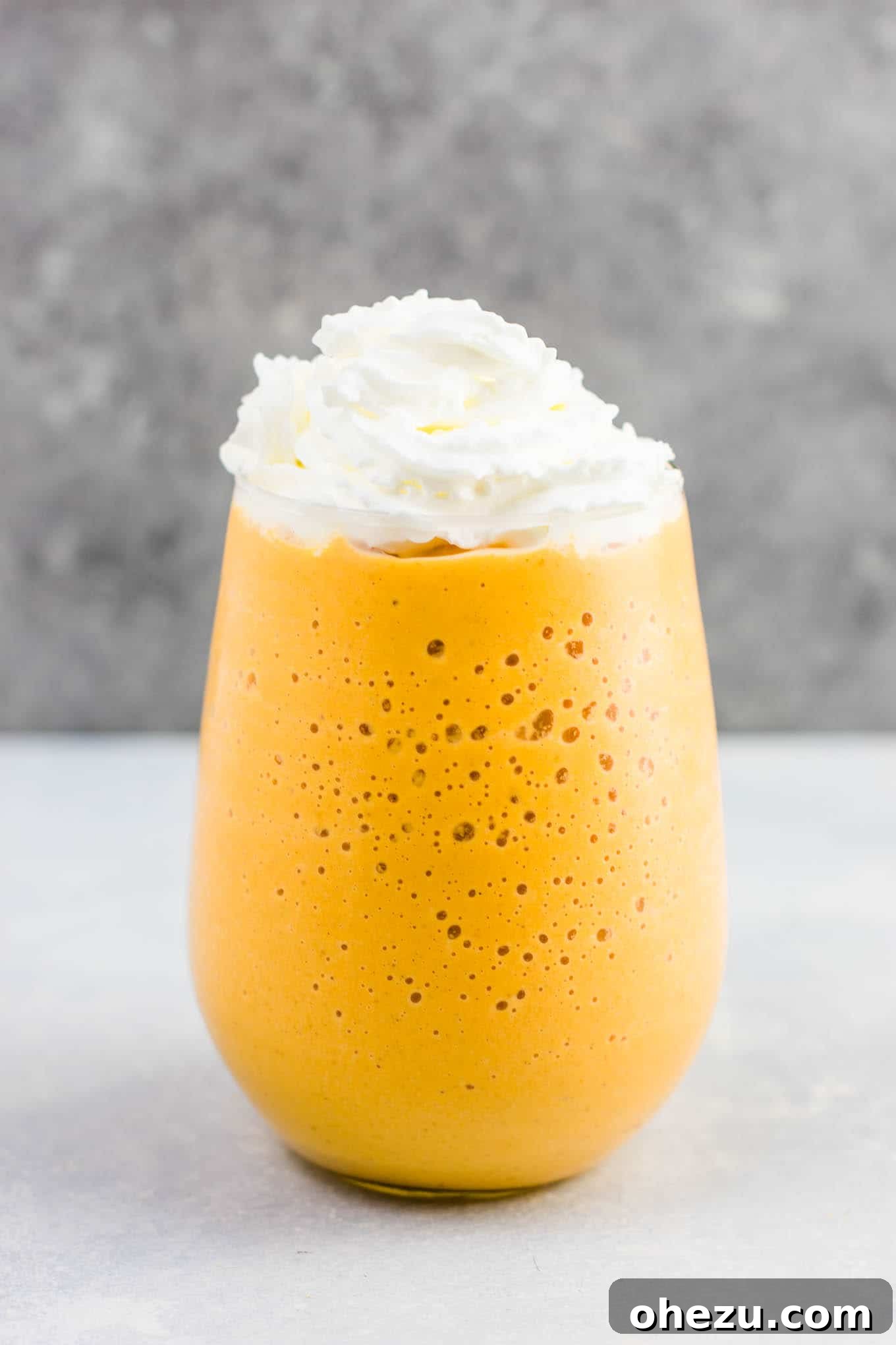 A glass of frozen pumpkin pie smoothie, beautifully topped with a swirl of whipped cream, inviting a taste.