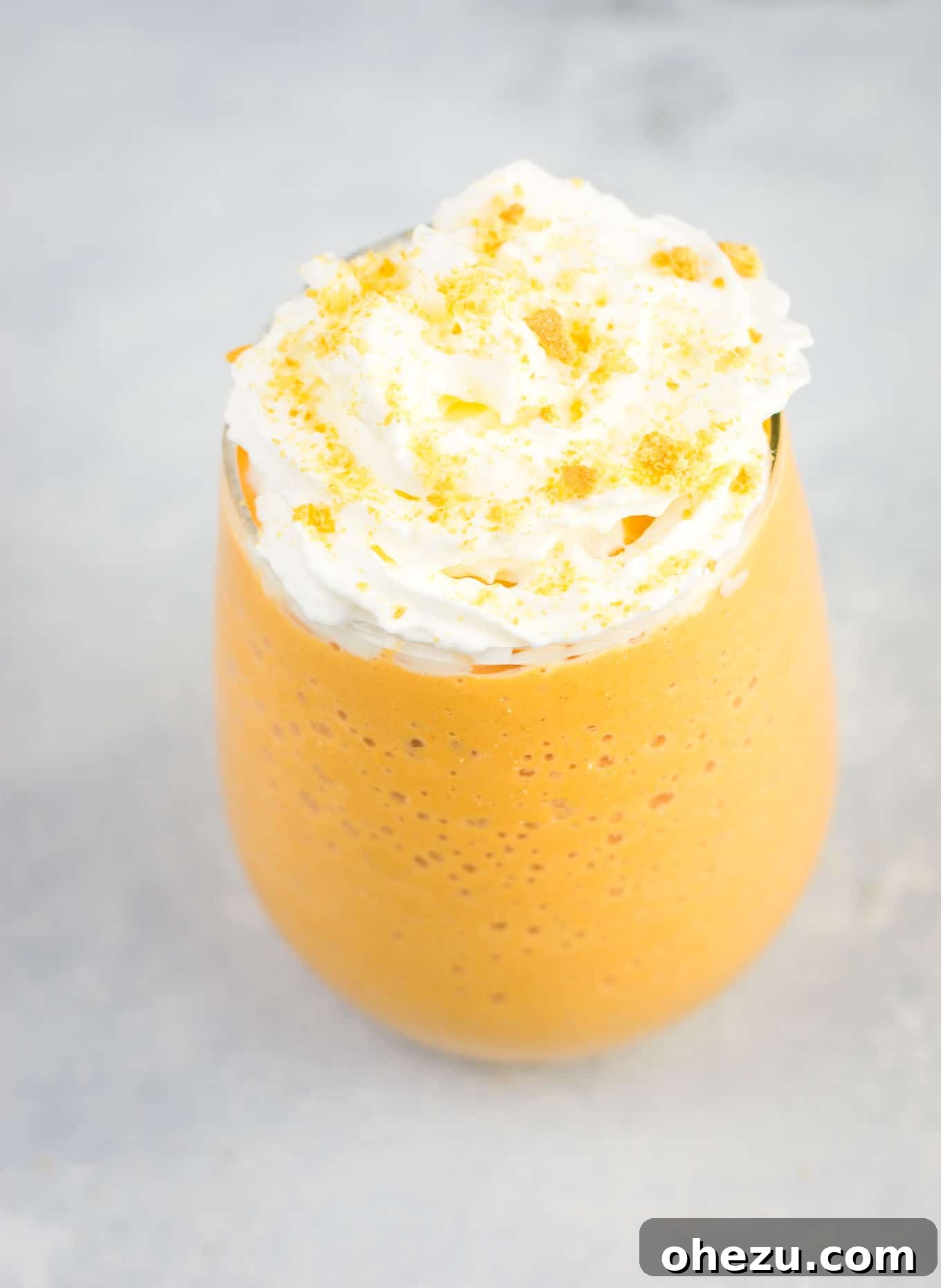 A frozen pumpkin pie smoothie in a glass, generously topped with whipped cream and crushed graham crackers, ready to be enjoyed as a perfect fall treat.