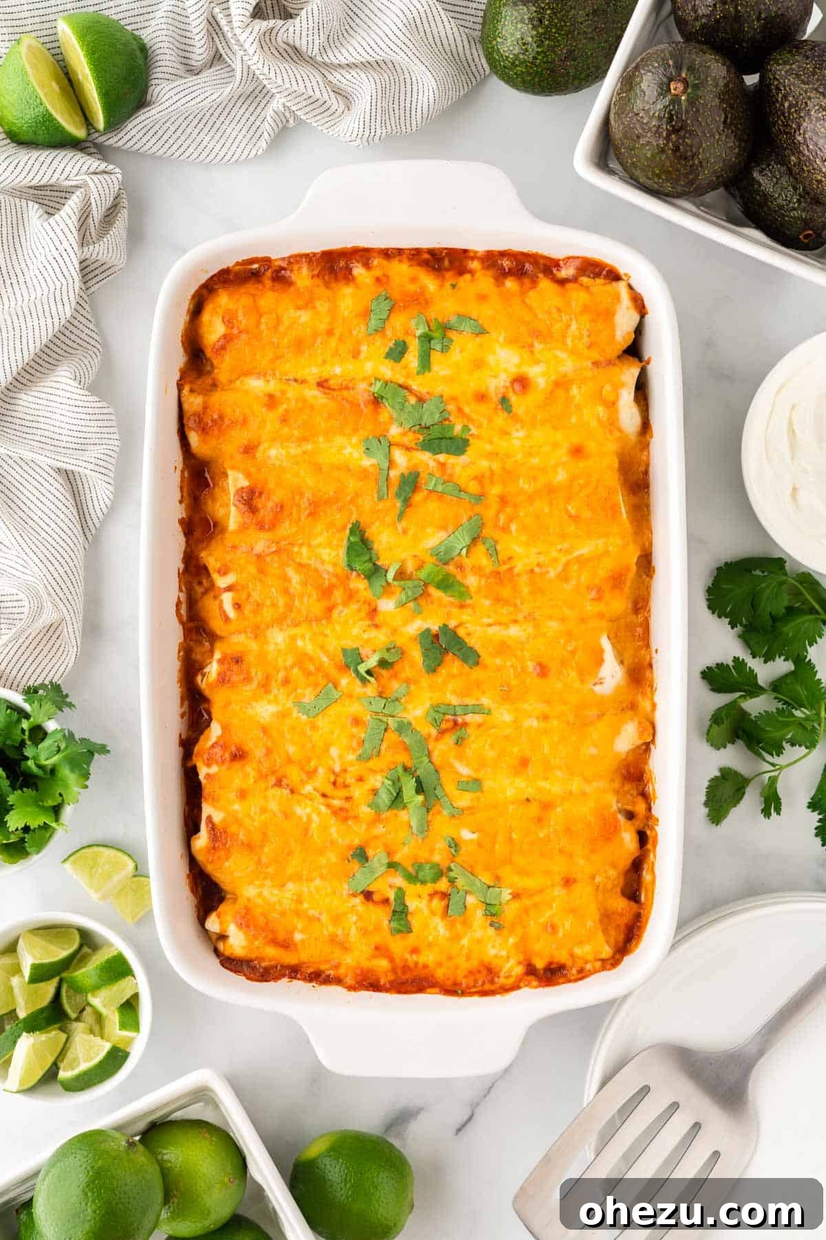 Two sweet potato black bean enchiladas on a white plate, garnished with fresh avocado, lime wedges, and sour cream.