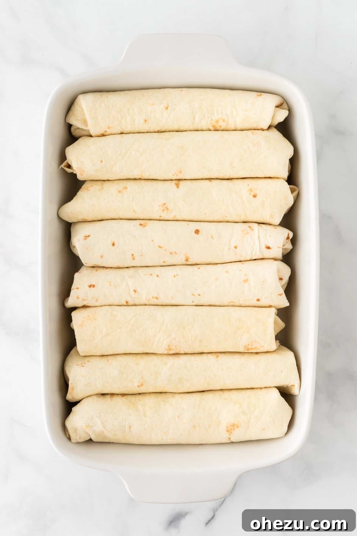 Several rolled-up enchiladas neatly arranged seam-side down in a 9x13 inch baking dish, ready for sauce and cheese.