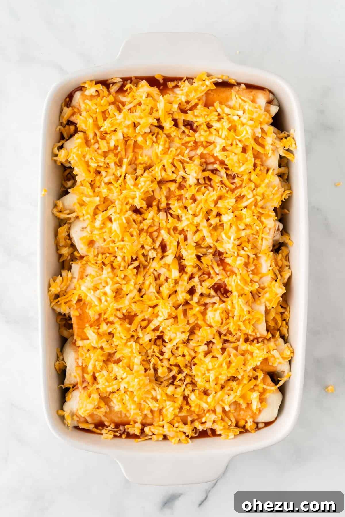 A generous layer of freshly grated Colby Jack cheese sprinkled over the enchilada sauce-covered rolls.
