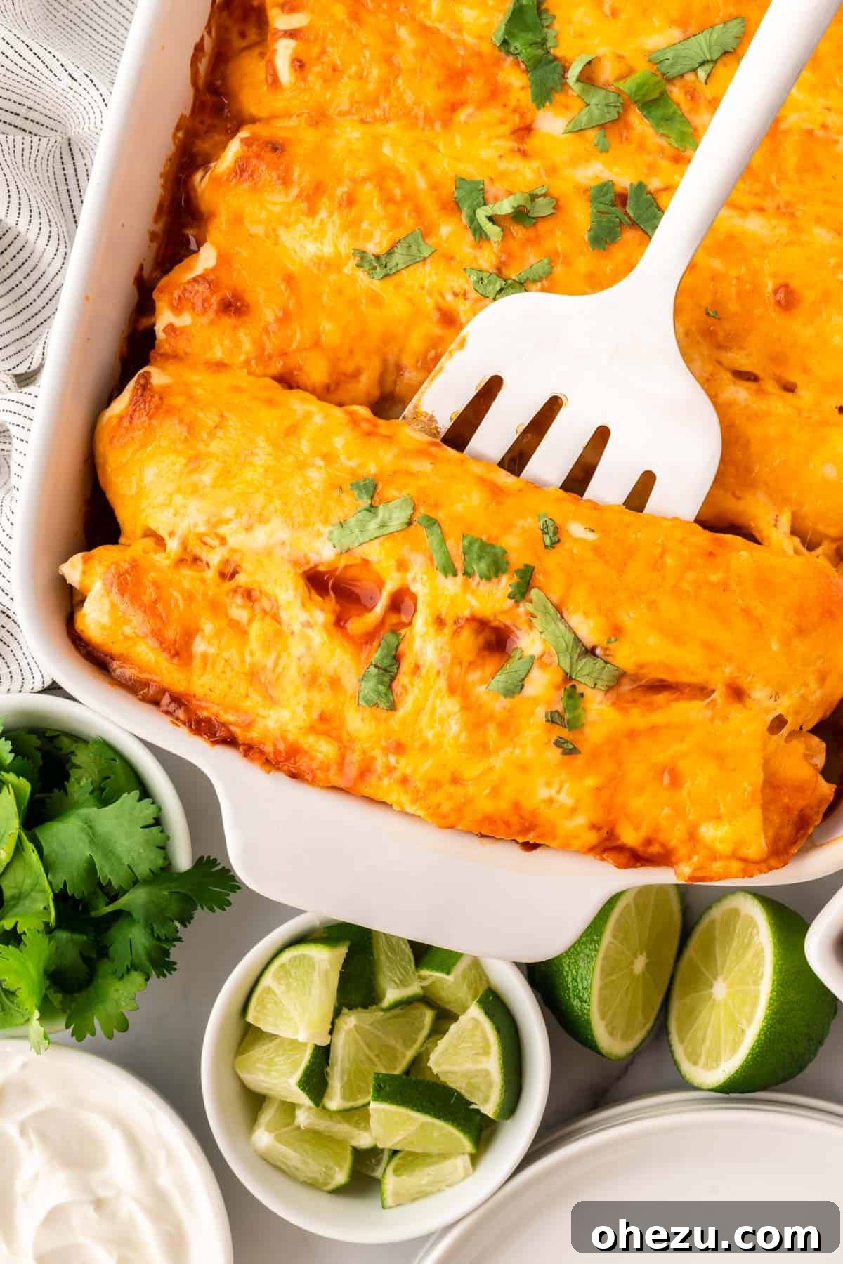 A spatula scooping a cheesy sweet potato black bean enchilada from the baking pan, showing the rich filling and sauce.