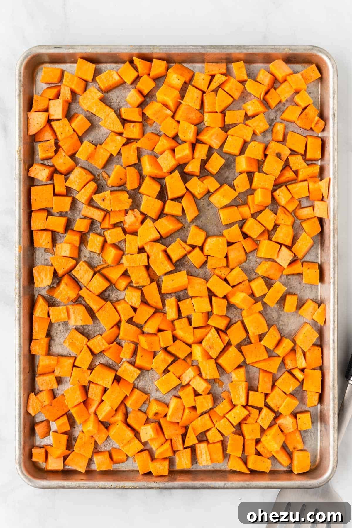 Diced sweet potato cubes spread on a baking sheet before roasting.