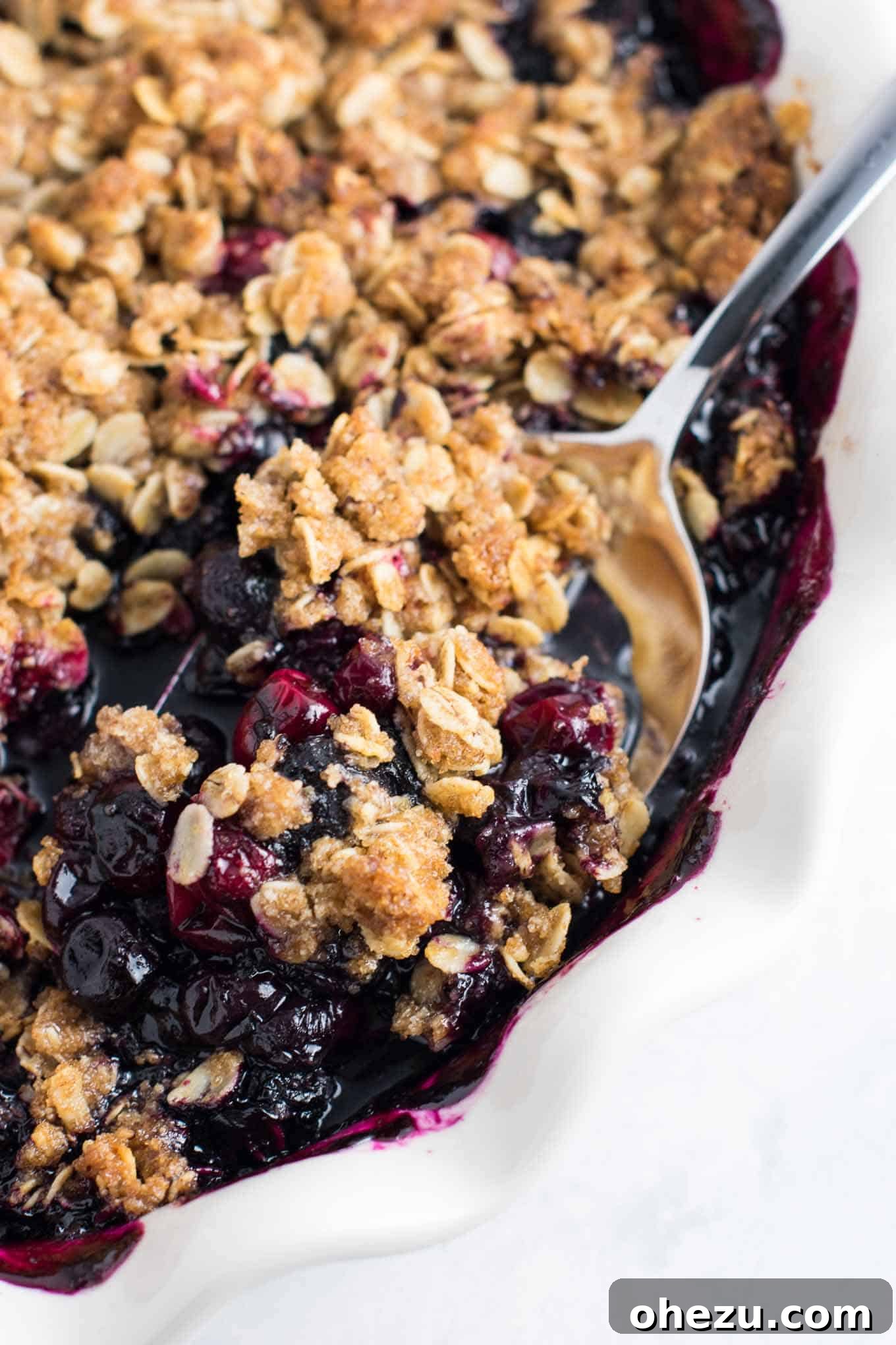 A spoon taking a generous scoop of warm cranberry blueberry crisp, showing its bubbly fruit filling and golden brown topping.