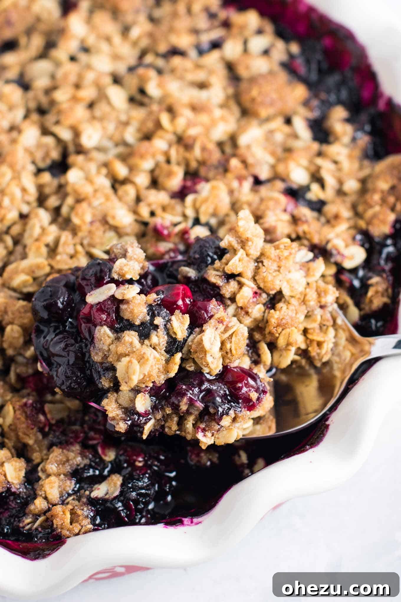 A spoon taking another mouth-watering scoop of cranberry blueberry crisp, highlighting its rich textures.