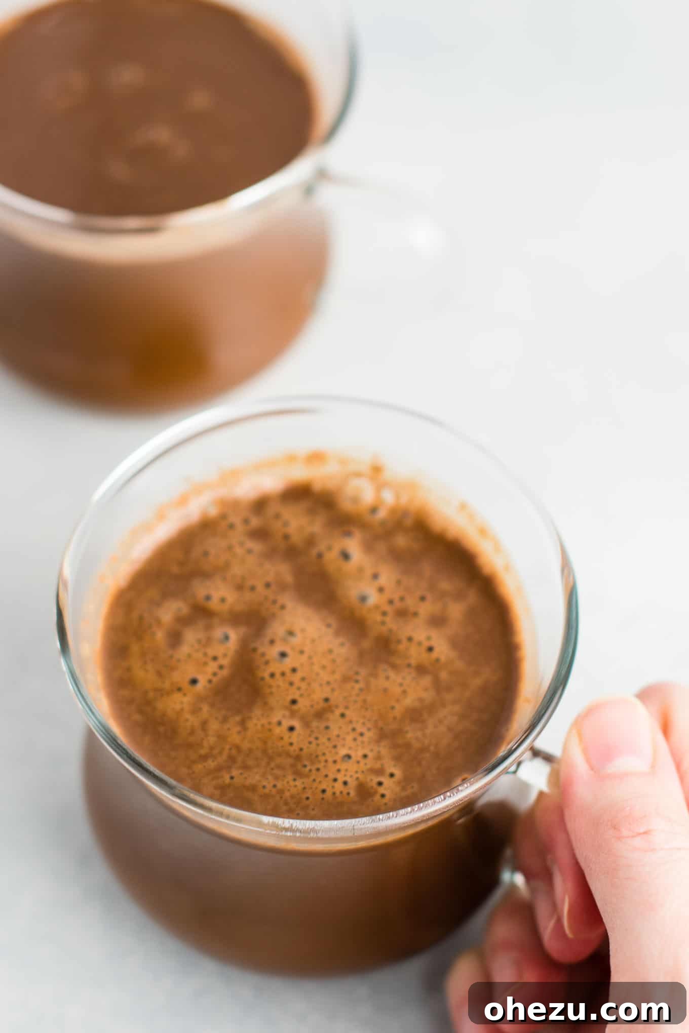 Close-up of the four simple ingredients for vegan hot chocolate: almond milk, dairy-free chocolate chips, cacao powder, and coconut palm sugar, neatly arranged on a white backdrop, highlighting their natural appeal.