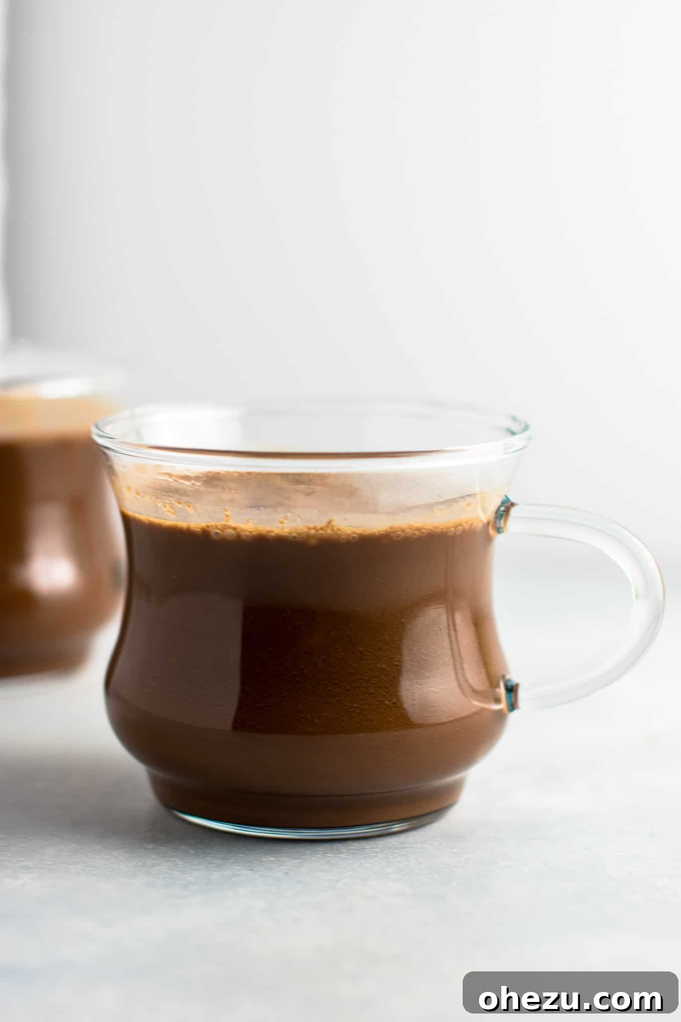 Two mugs of vegan hot chocolate, garnished with cinnamon sticks and a sprinkle of cacao, on a rustic wooden surface, exuding warmth and festive cheer, ready to be enjoyed during the holidays.