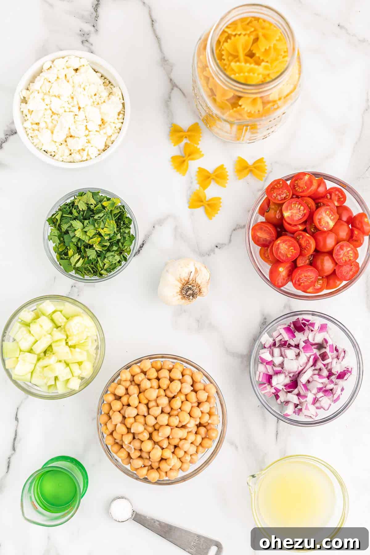 All the fresh ingredients for chickpea pasta salad laid out on a white surface
