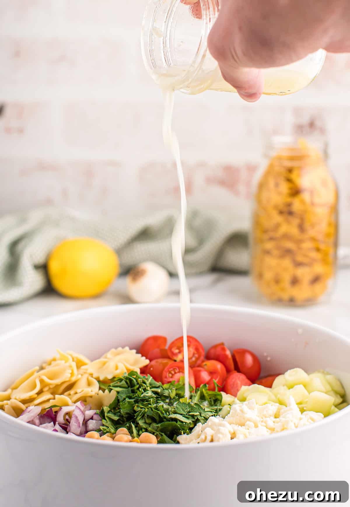 Pouring the lemon olive oil dressing over the mixed chickpea pasta salad ingredients