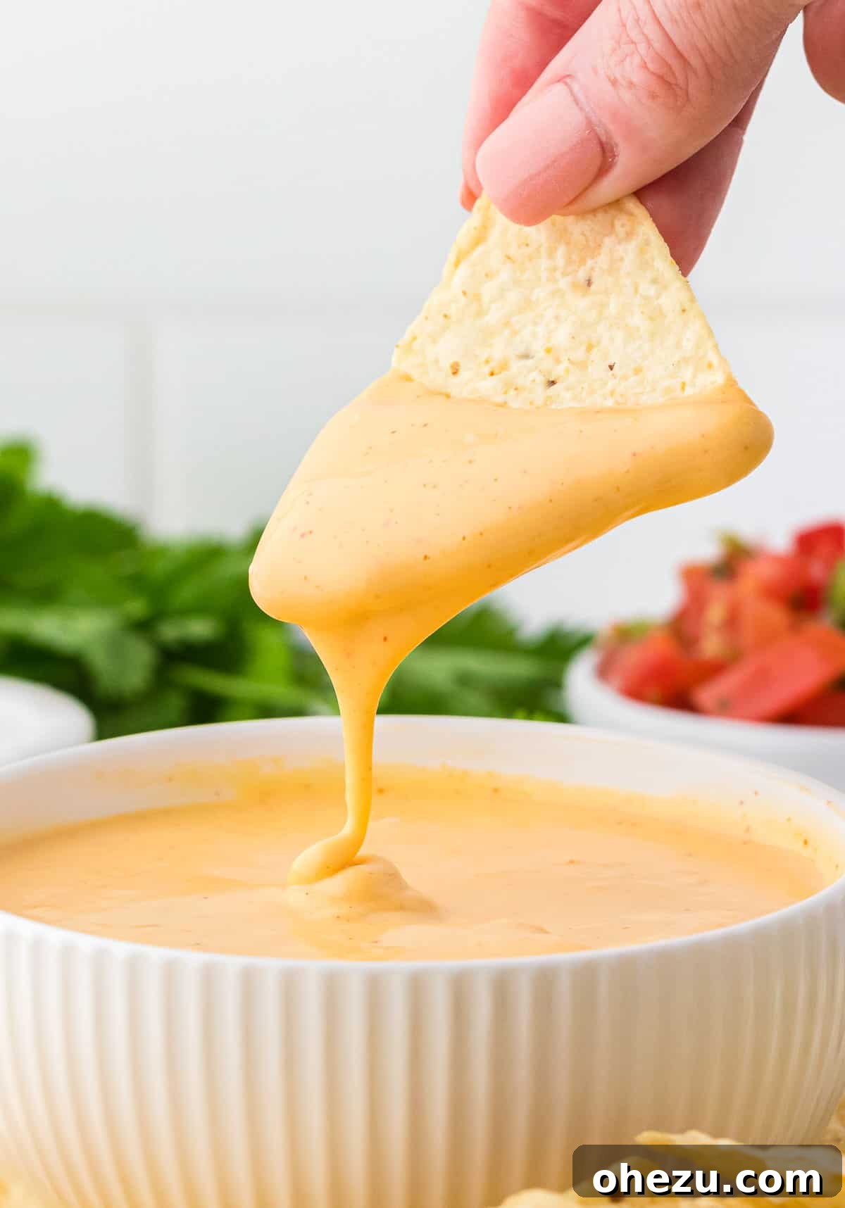 5-Minute Creamy Nacho Cheese Dip 11 A hand dipping a vibrant yellow tortilla chip into a swirling pool of rich, golden nacho cheese sauce, highlighting the sauce's creamy texture.