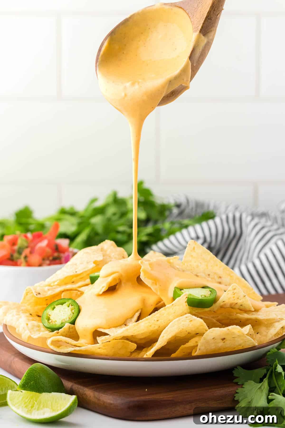 5-Minute Creamy Nacho Cheese Dip 12 A stream of golden, creamy nacho cheese sauce being poured from a small pitcher over a generously piled plate of crispy tortilla chips.