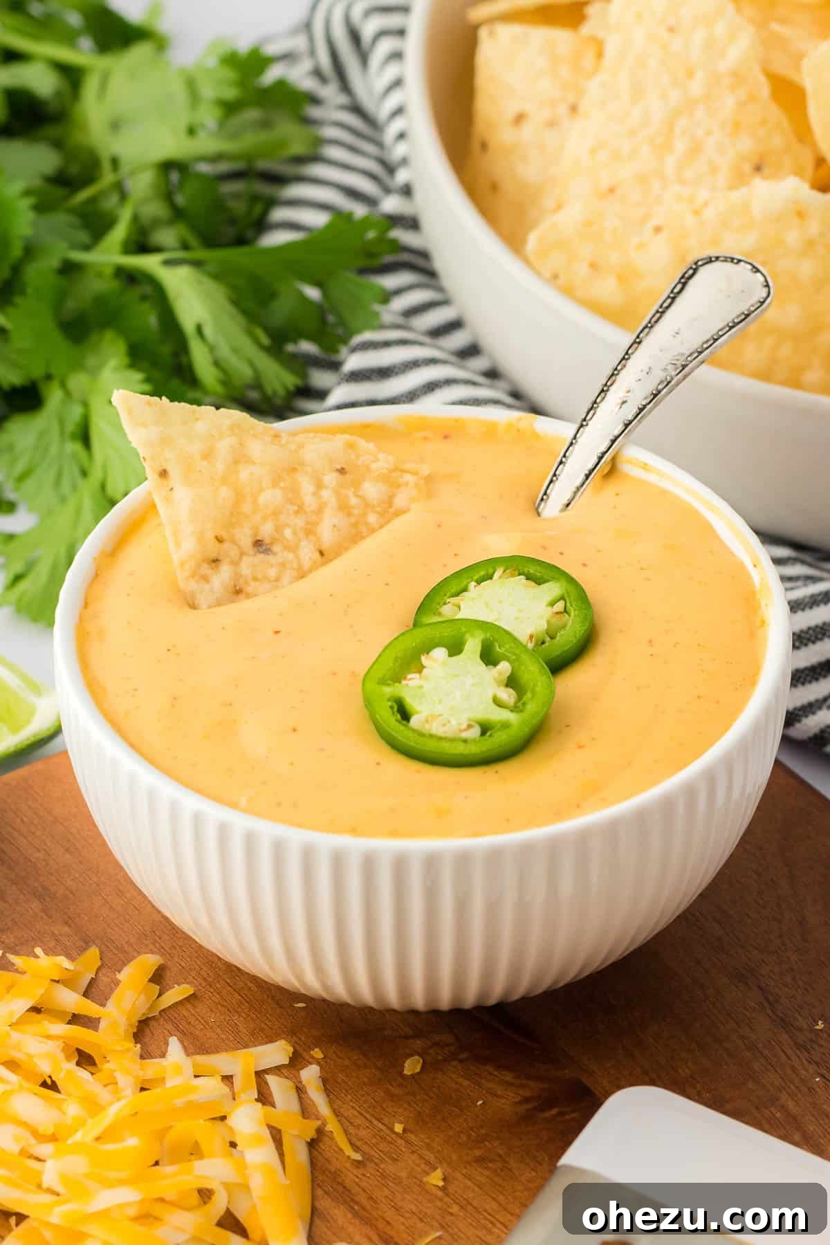 5-Minute Creamy Nacho Cheese Dip 15 Two separate bowls of nacho cheese sauce, one plain and the other topped with several slices of jalapeño, showcased against a light background.