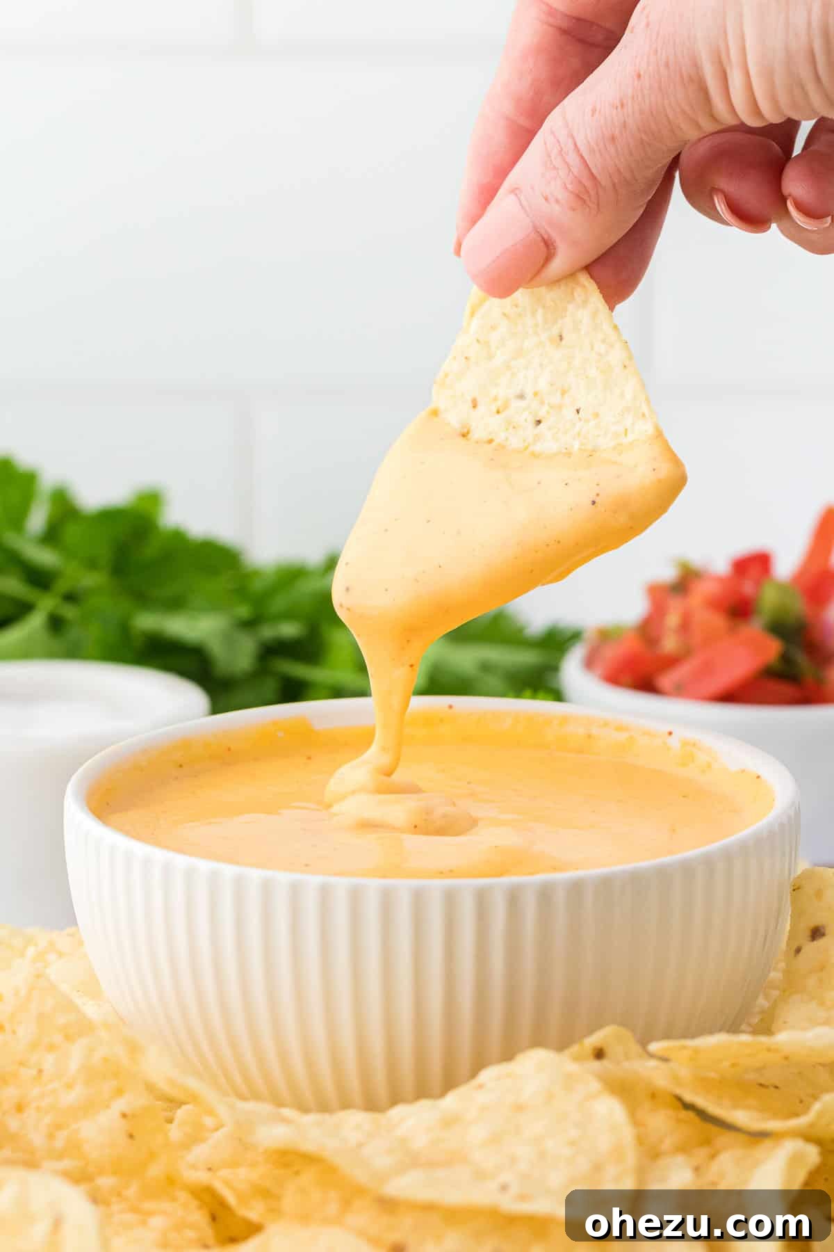 5-Minute Creamy Nacho Cheese Dip 16 A hand reaching into a bowl of creamy nacho cheese sauce with a tortilla chip, ready for a delicious bite.