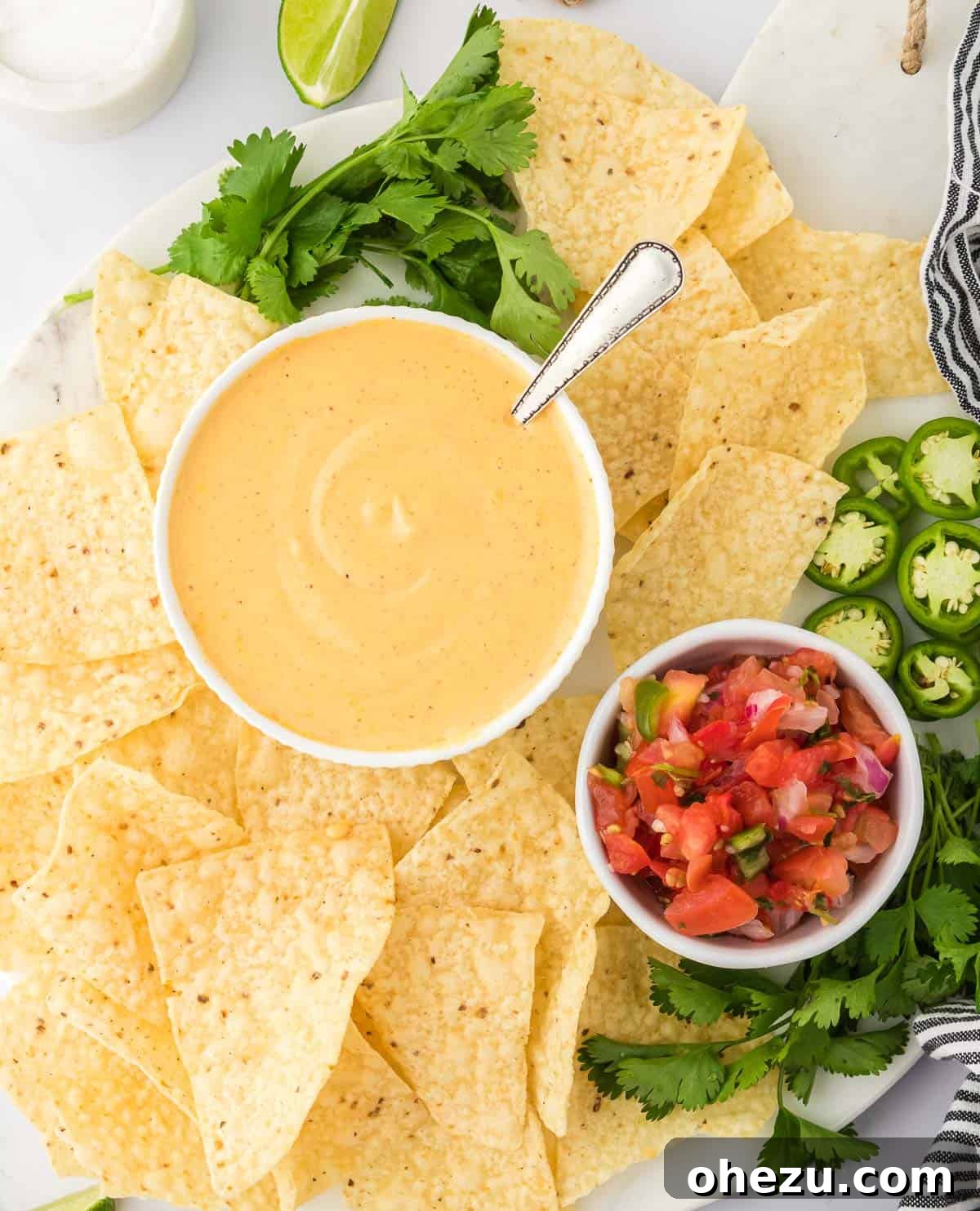 5-Minute Creamy Nacho Cheese Dip 3 A deep bowl of golden nacho cheese sauce garnished with a sprig of cilantro, surrounded by a scattering of crispy tortilla chips on a rustic wooden board.