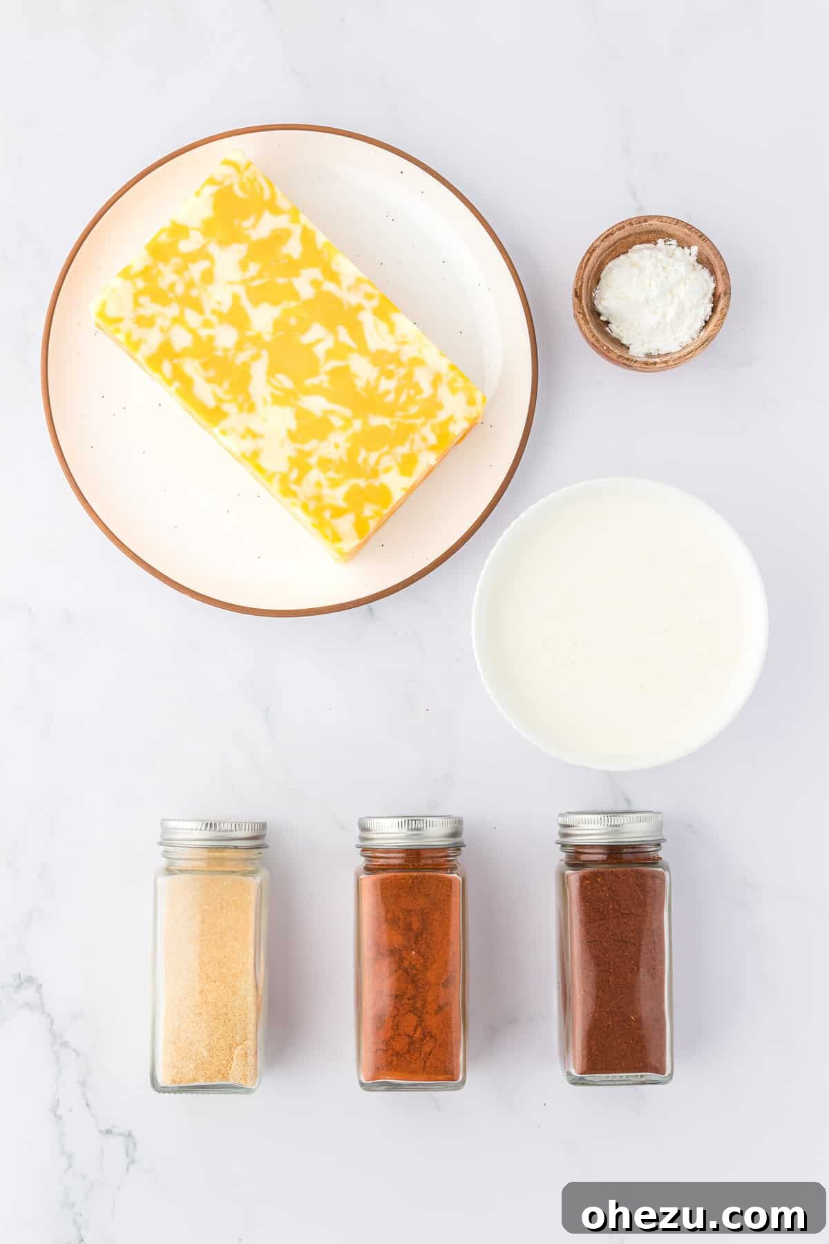 5-Minute Creamy Nacho Cheese Dip 4 A collection of ingredients laid out on a dark surface, including a block of Colby Jack cheese, heavy cream, and small bowls of paprika, chili powder, and garlic powder, ready for making nacho cheese.