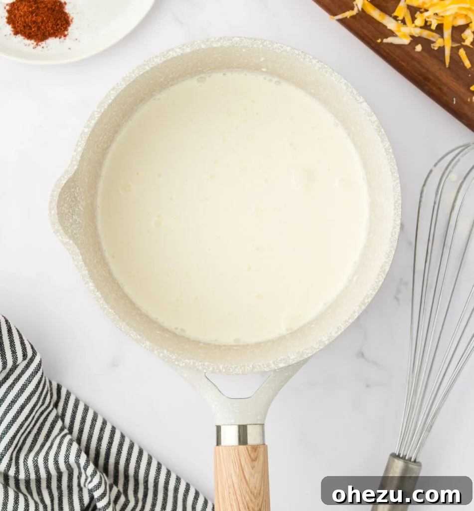 5-Minute Creamy Nacho Cheese Dip 5 Heavy cream gently simmering in a metal saucepan on a stove, showing the start of the cheese sauce process.