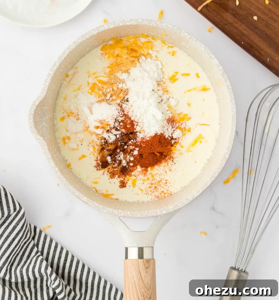 5-Minute Creamy Nacho Cheese Dip 6 Various ingredients, including shredded cheese, red spices, and white powder, are mixed into warm heavy cream in a saucepan with a spatula.
