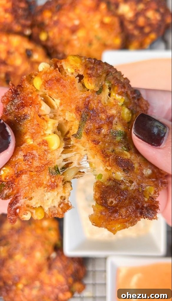 Golden brown cheesy corn fritters on a plate, garnished with fresh herbs, ready to be served.