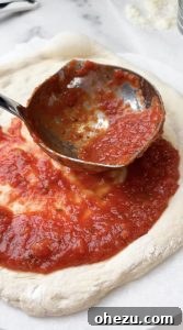 Applying pizza sauce to dough on a wooden peel