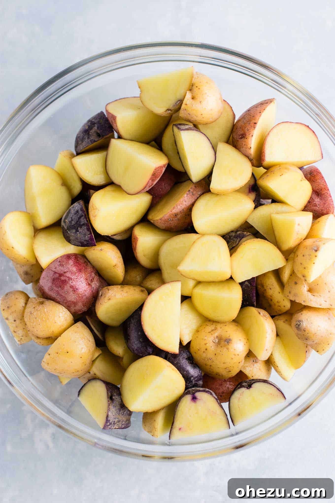 An array of baby potatoes in vibrant mixed colors, quartered and ready for seasoning in a bowl.