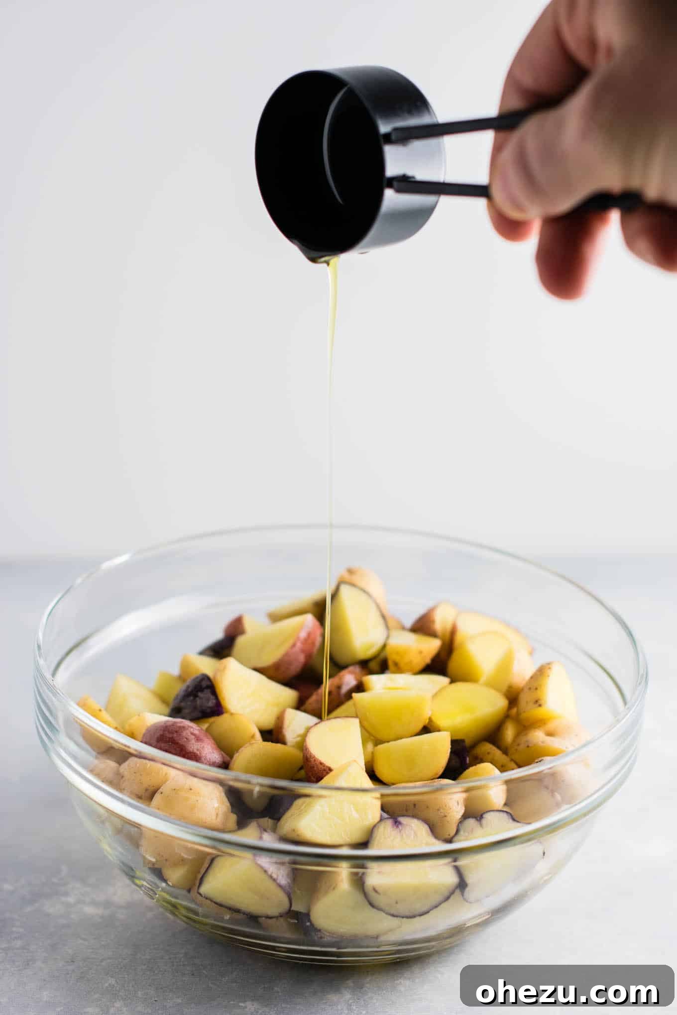 Quartered baby potatoes tossed with olive oil, sea salt, pepper, garlic powder, and parmesan cheese in a mixing bowl.