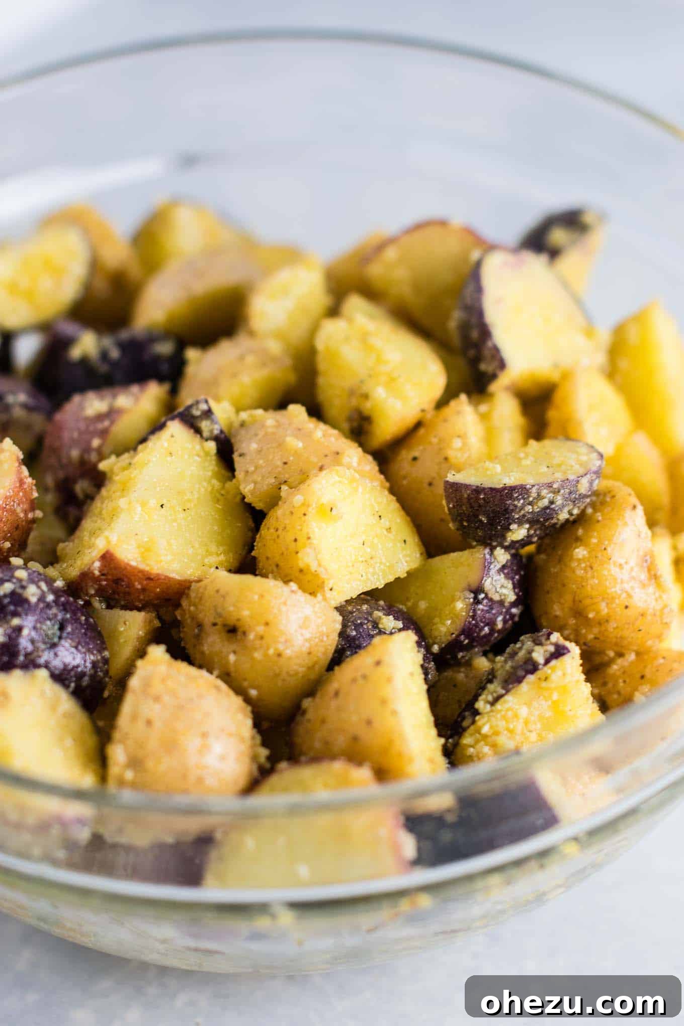 Seasoned and coated garlic parmesan potatoes, evenly spread on a baking sheet, ready to go into the oven.