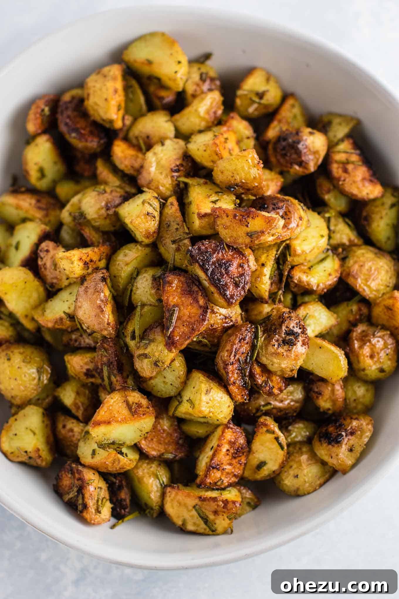 A vibrant platter of golden-brown rosemary roasted potatoes, glistening with olive oil and fresh rosemary sprigs.