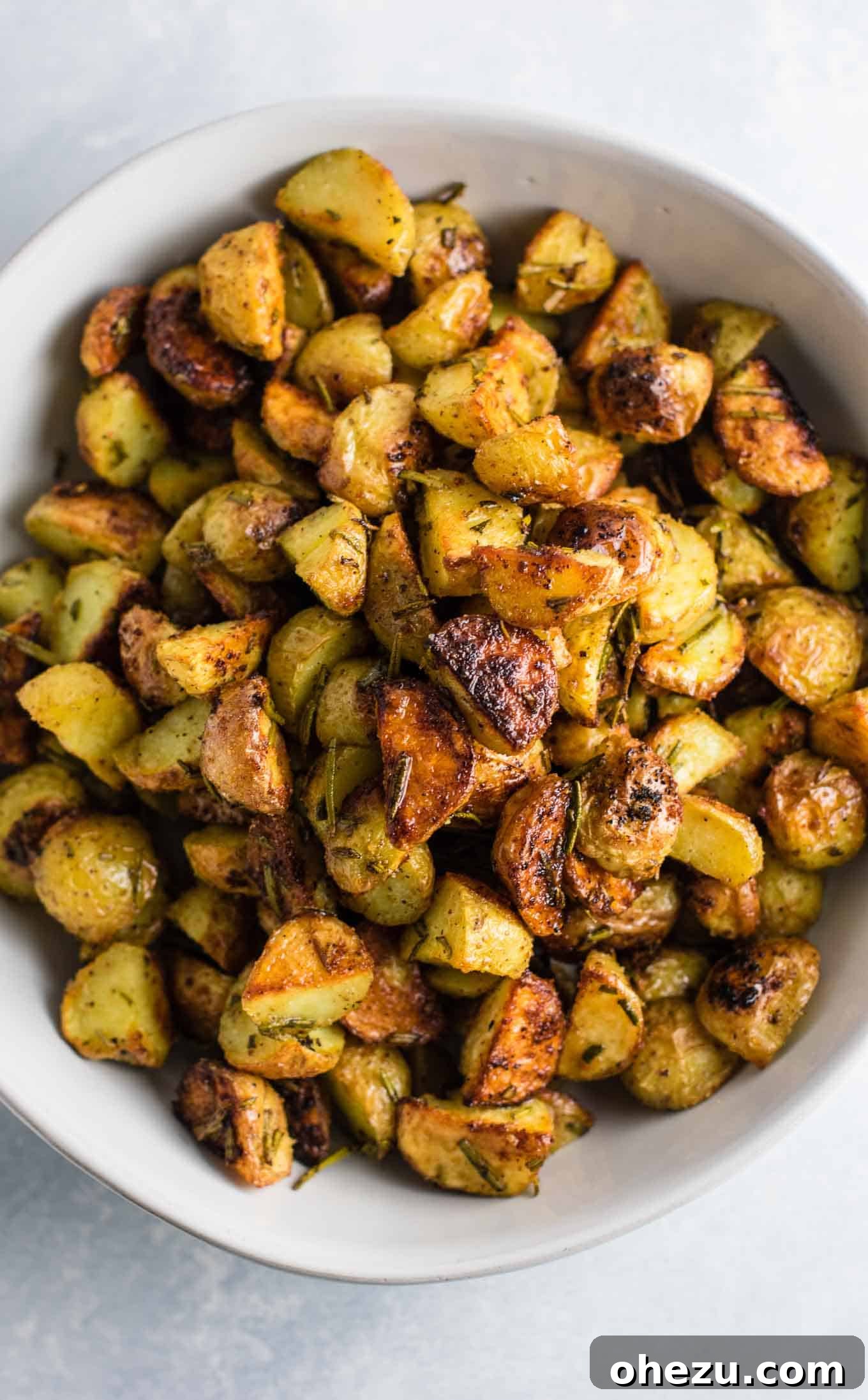 A close-up of a rustic wooden bowl filled with beautifully golden and crispy rosemary roasted potatoes, garnished with fresh rosemary.