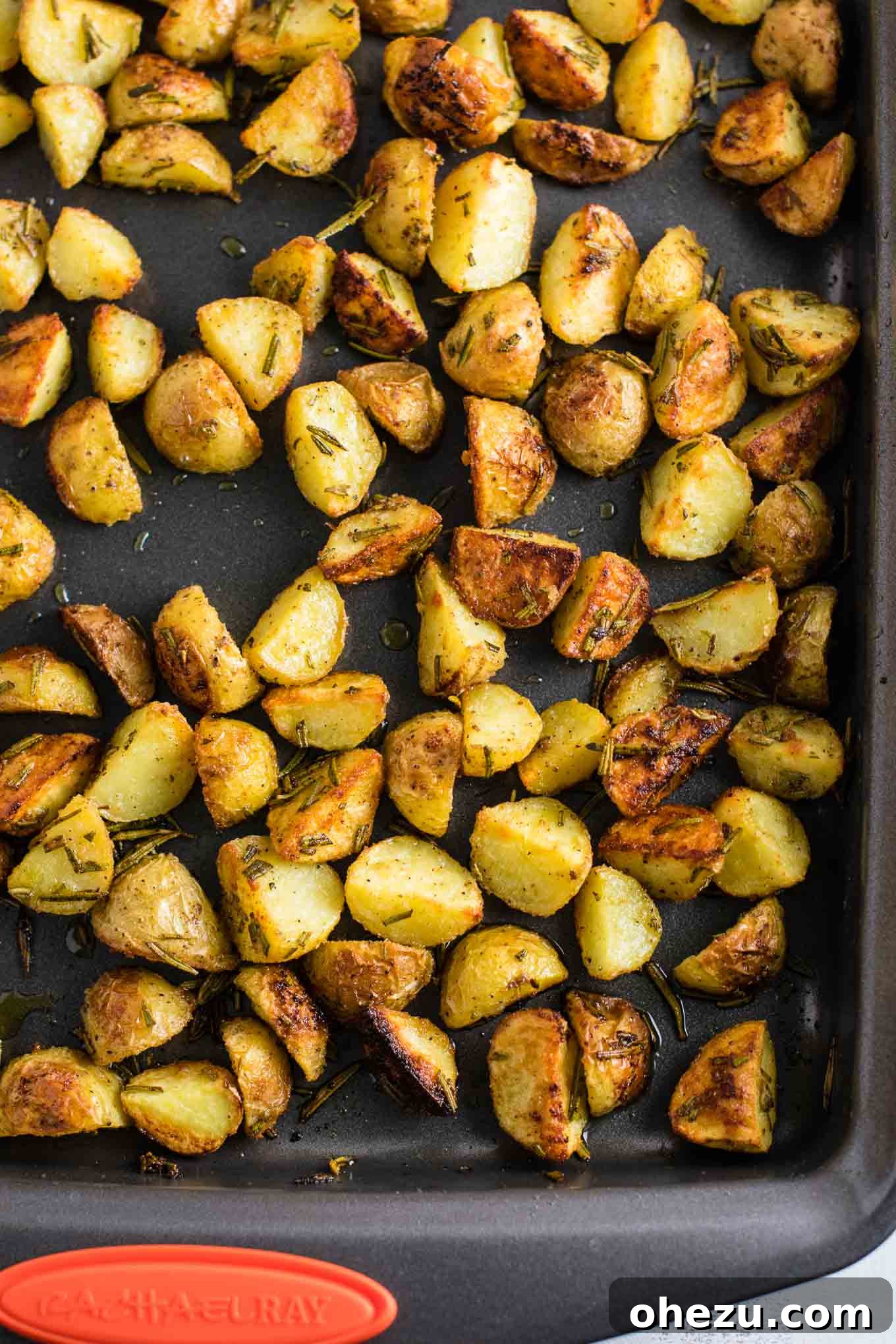 Raw baby potatoes, perfectly quartered and seasoned with fresh rosemary and various spices, laid out on a baking sheet before roasting.