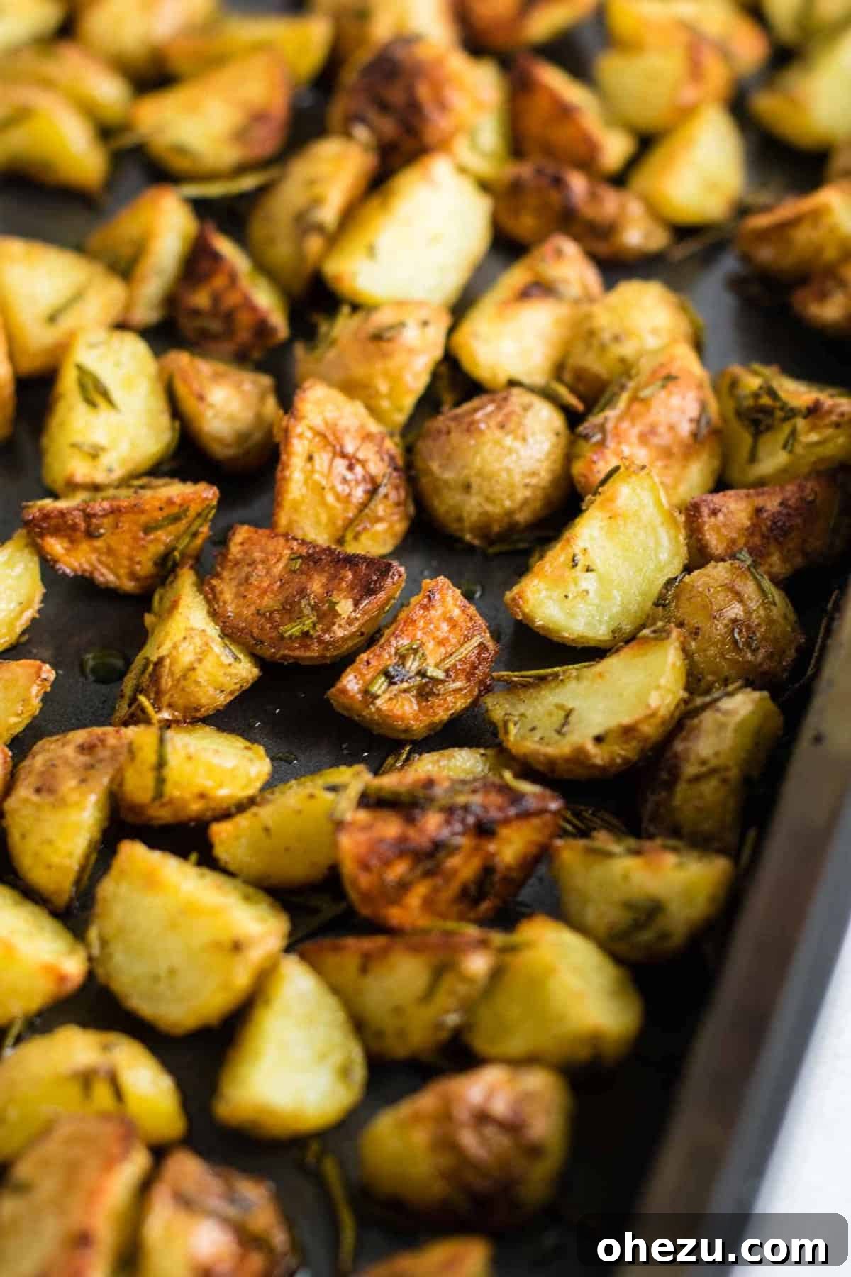 A close-up shot of raw, quartered baby potatoes mixed with freshly chopped rosemary and seasonings in a mixing bowl, ready to be coated with olive oil.