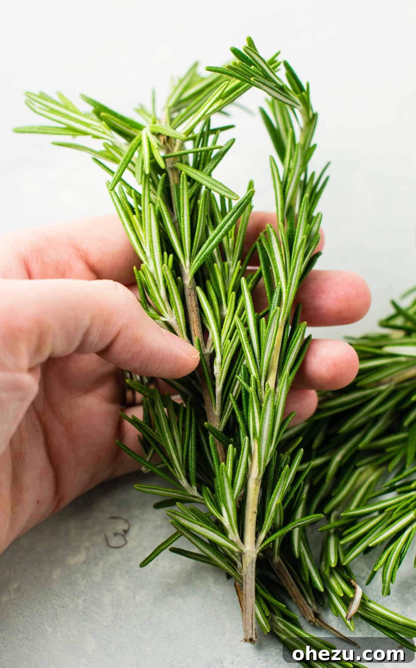 Fresh rosemary sprigs being finely chopped on a wooden cutting board, releasing their fragrant aroma.