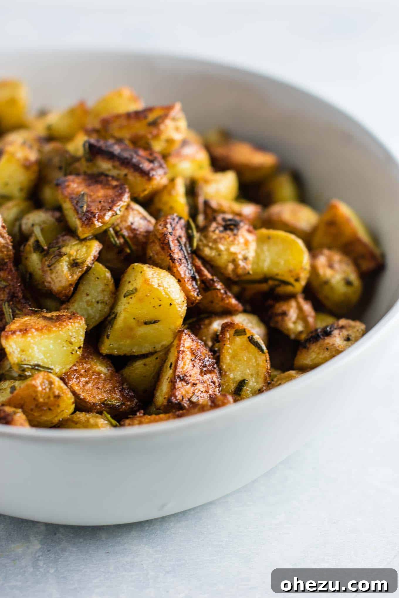A serving of crispy rosemary roasted potatoes on a plate, with a side of ketchup for dipping.