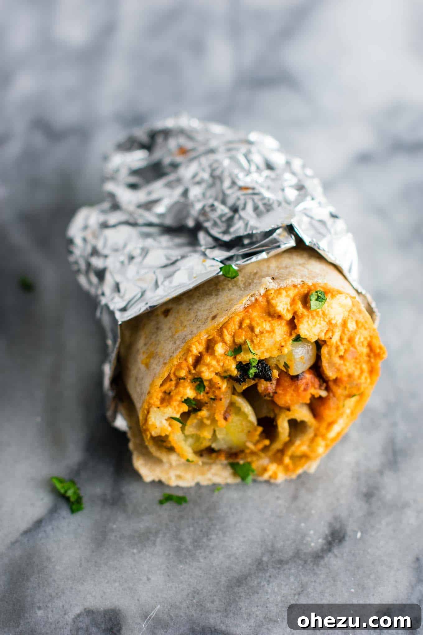 A vegan breakfast burrito, half-wrapped in foil, showing its hearty filling