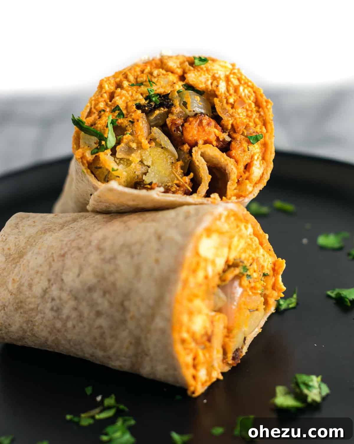 Two halves of a perfectly rolled and cut vegan breakfast burrito, showing the generous filling