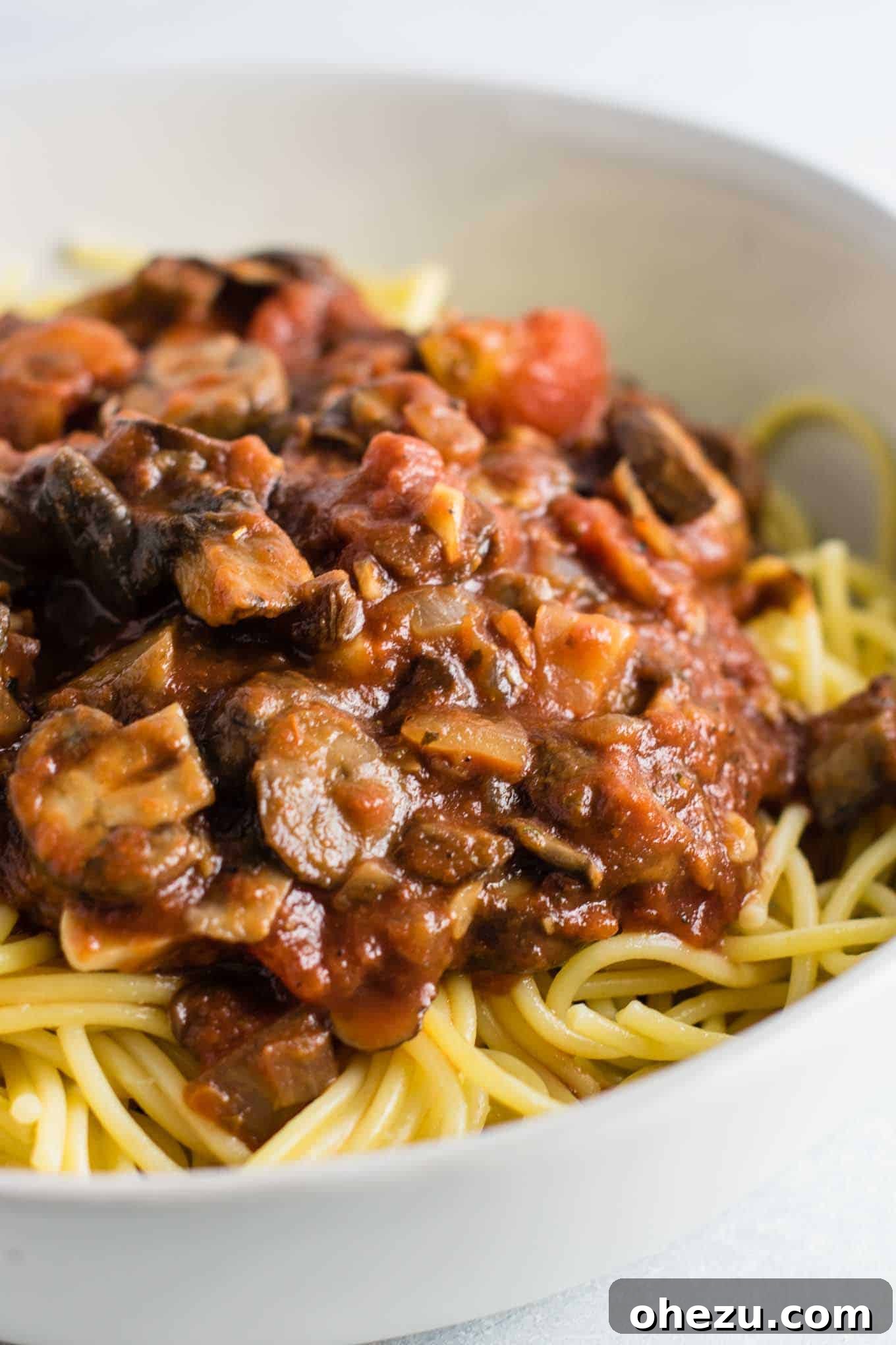 Flavorful vegan spaghetti sauce served generously over perfectly cooked white spaghetti noodles in a rustic white bowl, garnished with fresh basil.