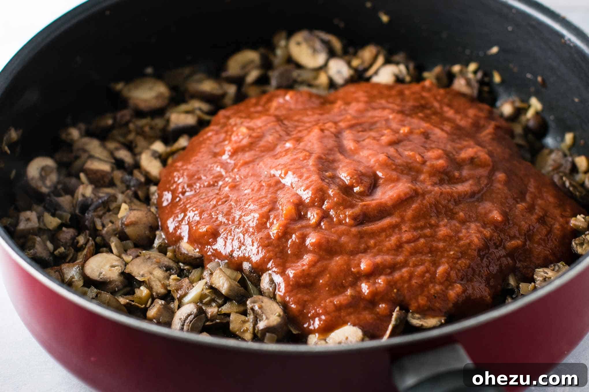 Vibrant pasta sauce spread evenly over the sautéed mushrooms, garlic, and onions in a skillet, ready for a gentle simmer.