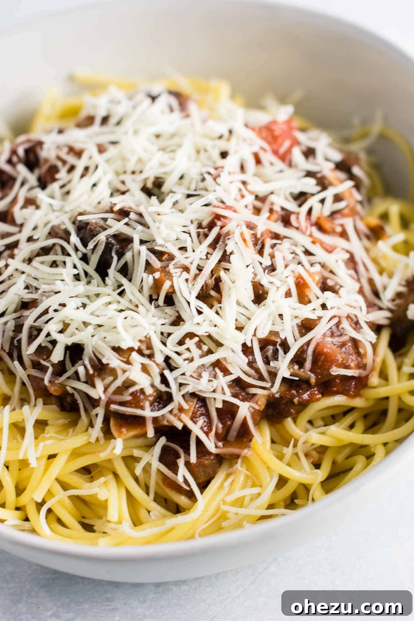 A bowl of spaghetti topped with rich meatless sauce, generously sprinkled with shredded mozzarella cheese, ready for baking or serving.