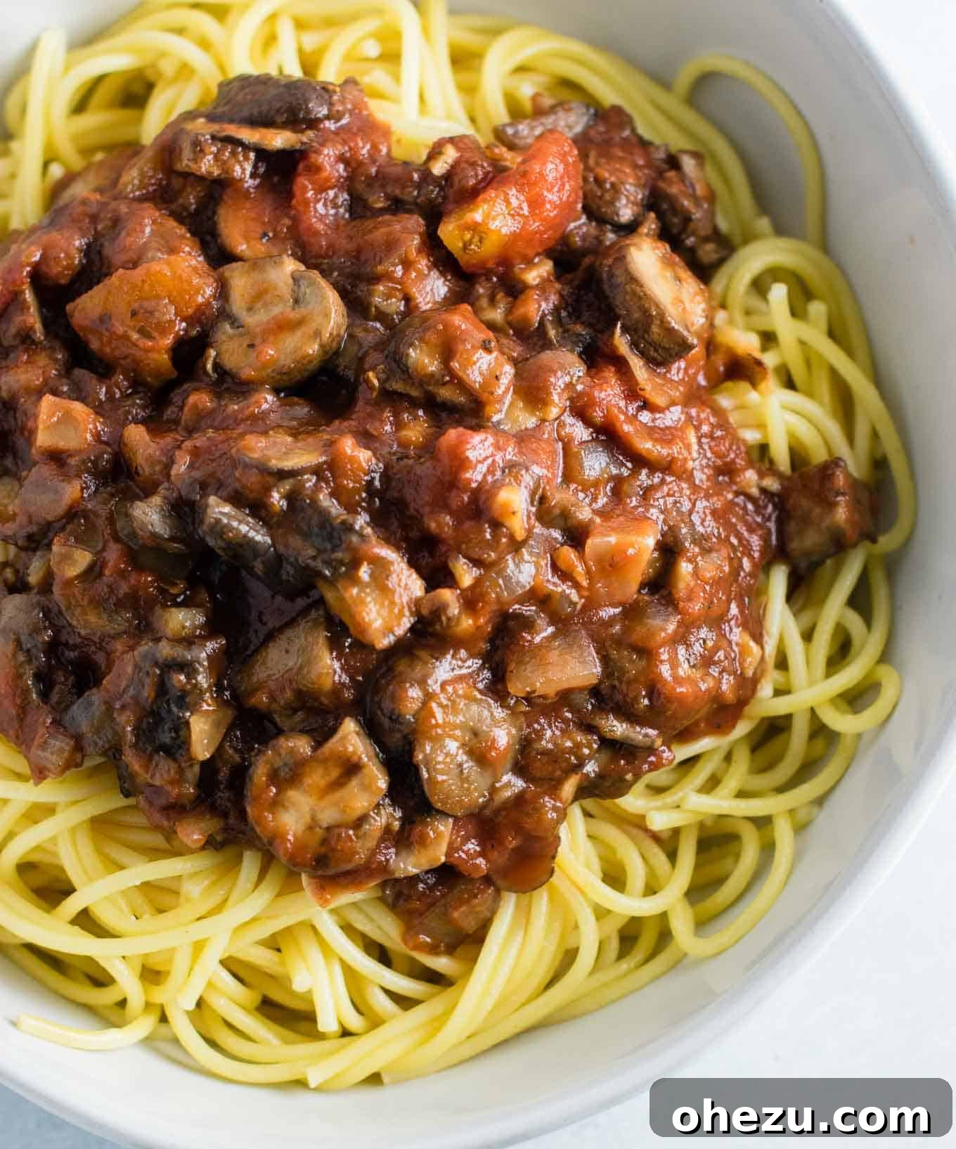 Hearty vegetarian mushroom spaghetti sauce generously coating white spaghetti noodles in an elegant white bowl, ready to be enjoyed.