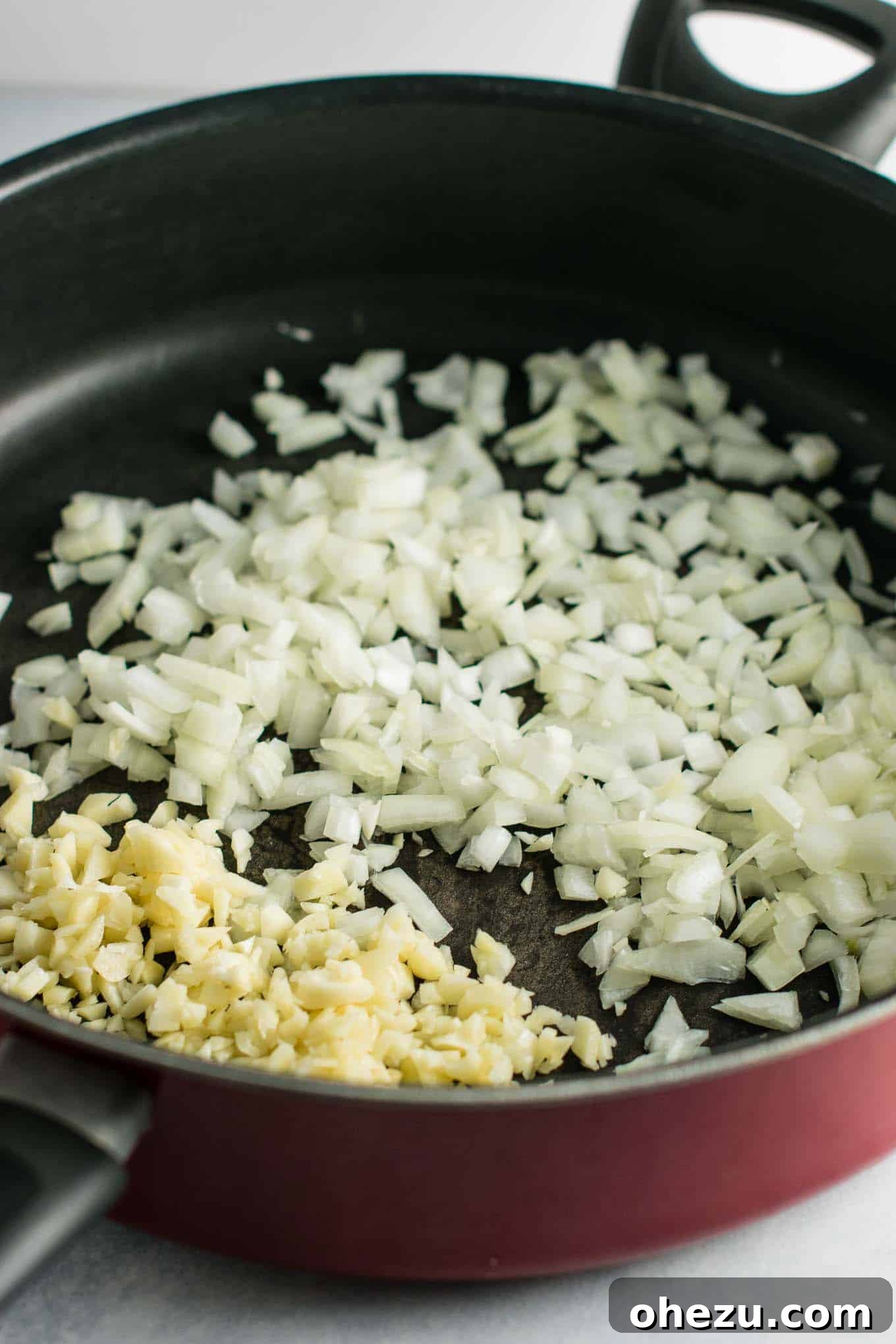 Finely chopped yellow onion and freshly minced garlic cloves sitting in a large, well-seasoned skillet, ready for sautéing.