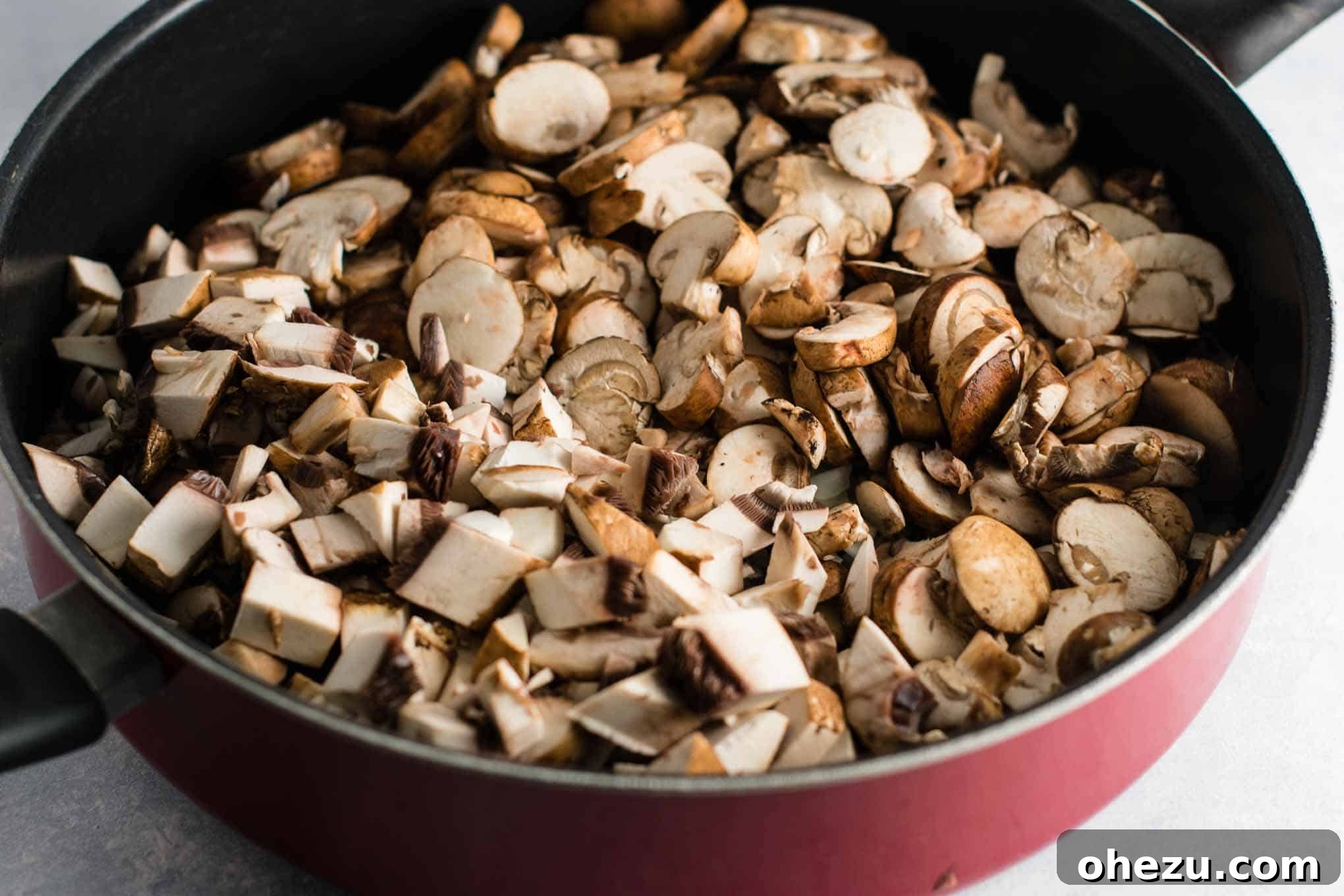 A generous quantity of freshly sliced baby bella mushrooms combined with diced portobello mushroom caps in a bowl, prepared for addition to the sauce.