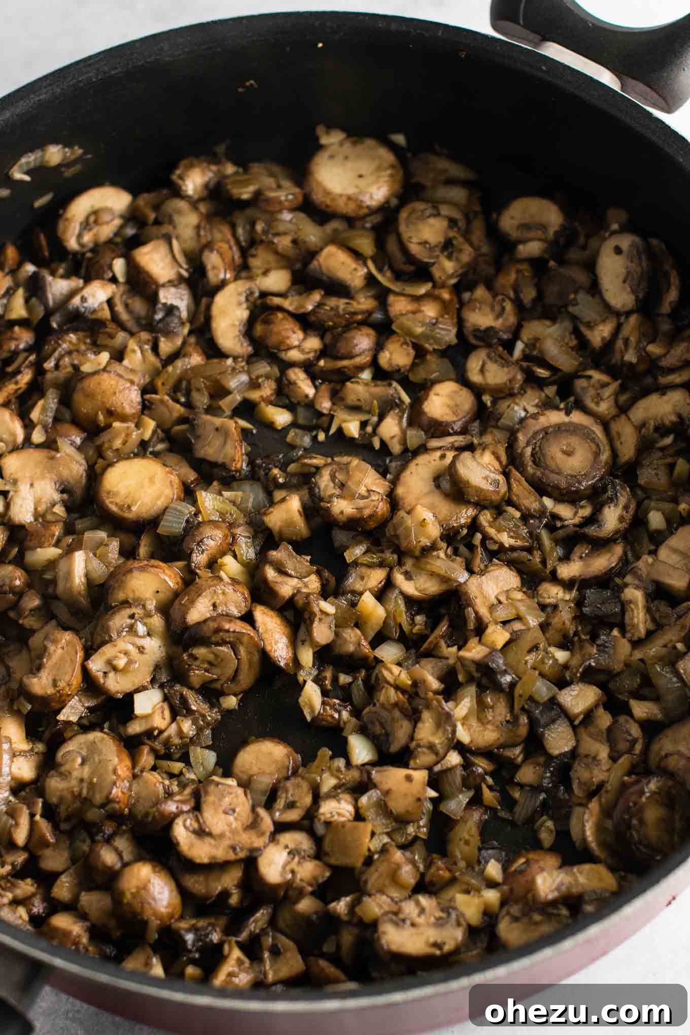 A close-up of browned mushrooms, garlic, and onion mixture after thorough cooking in a skillet, showing the reduced liquid and rich, caramelized tones.