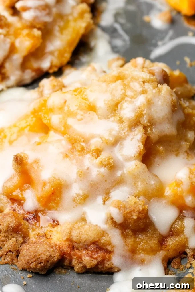 Freshly baked peach cobbler cinnamon rolls cooling on a wire rack, glistening with glaze