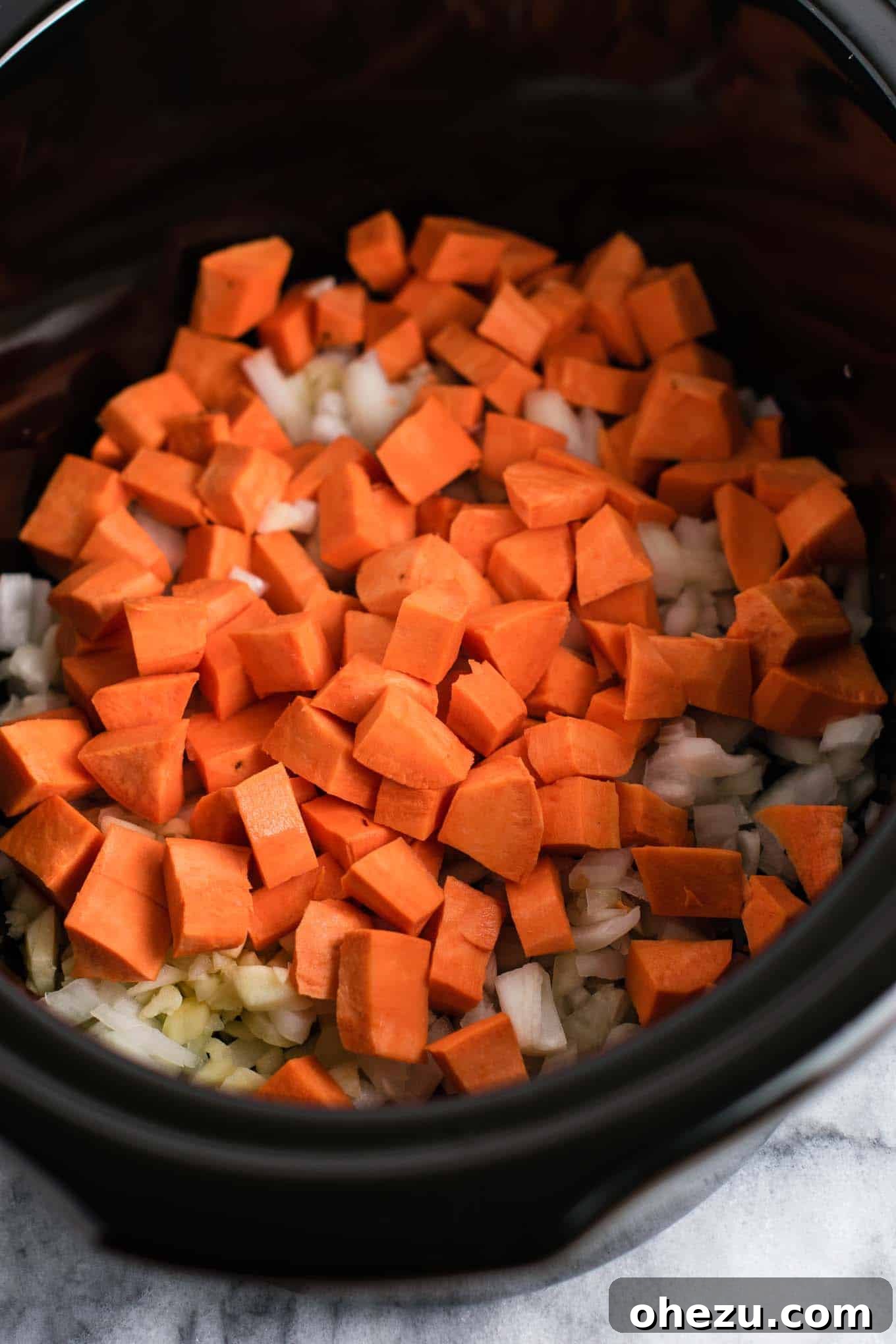 Effortless Plant-Based Sweet Potato Chili in Your Slow Cooker 4 Diced sweet potatoes, minced garlic, and chopped onions piled together, forming the aromatic base for the slow cooker vegetarian chili.
